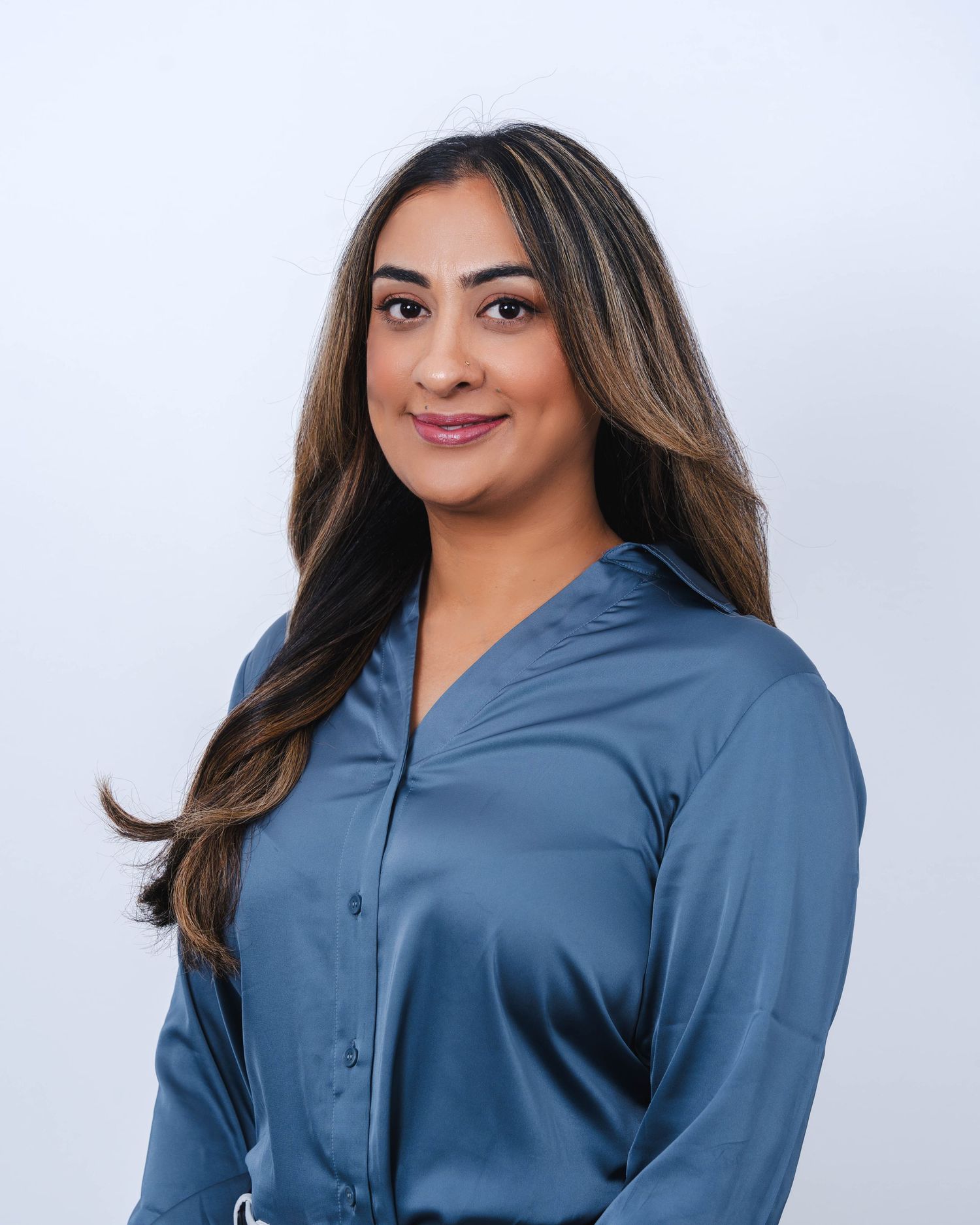 Professional headshot of someone wearing a blue button-up shirt against a light gray background.