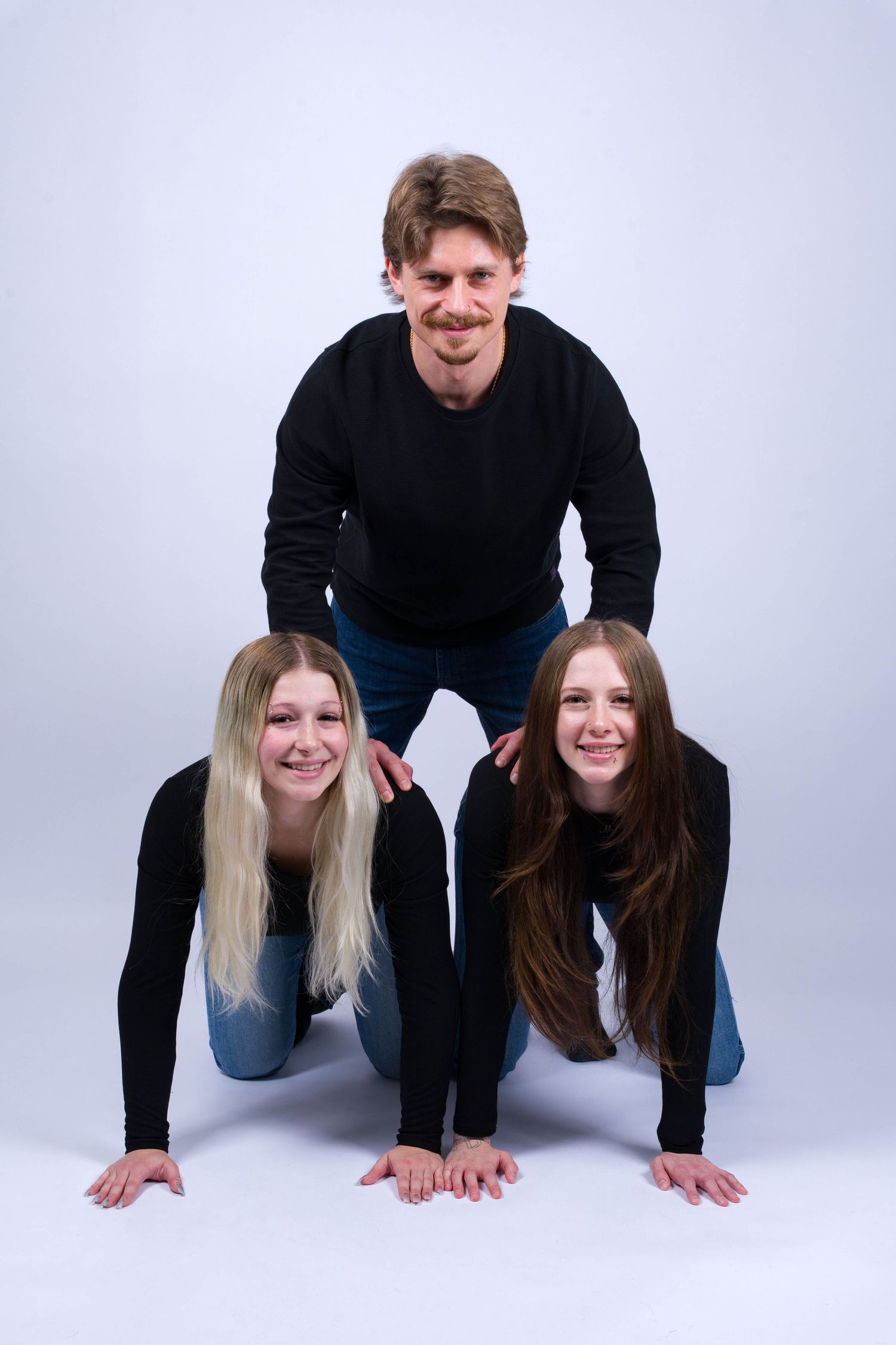 People in black tops posing on hands and knees in a playful studio photoshoot sequence.