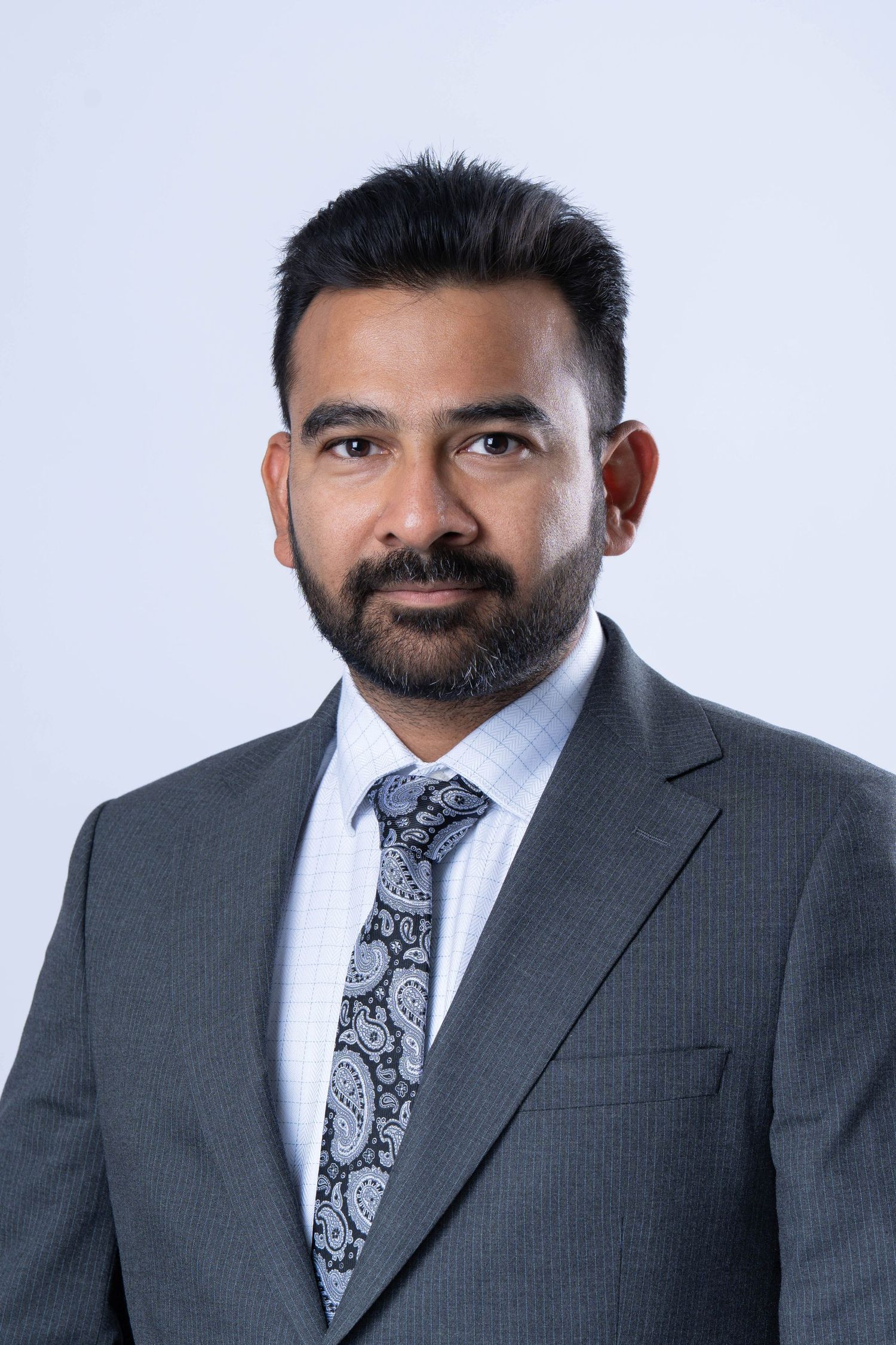 Professional headshot series of a bearded man in a gray suit and patterned tie against a light background.