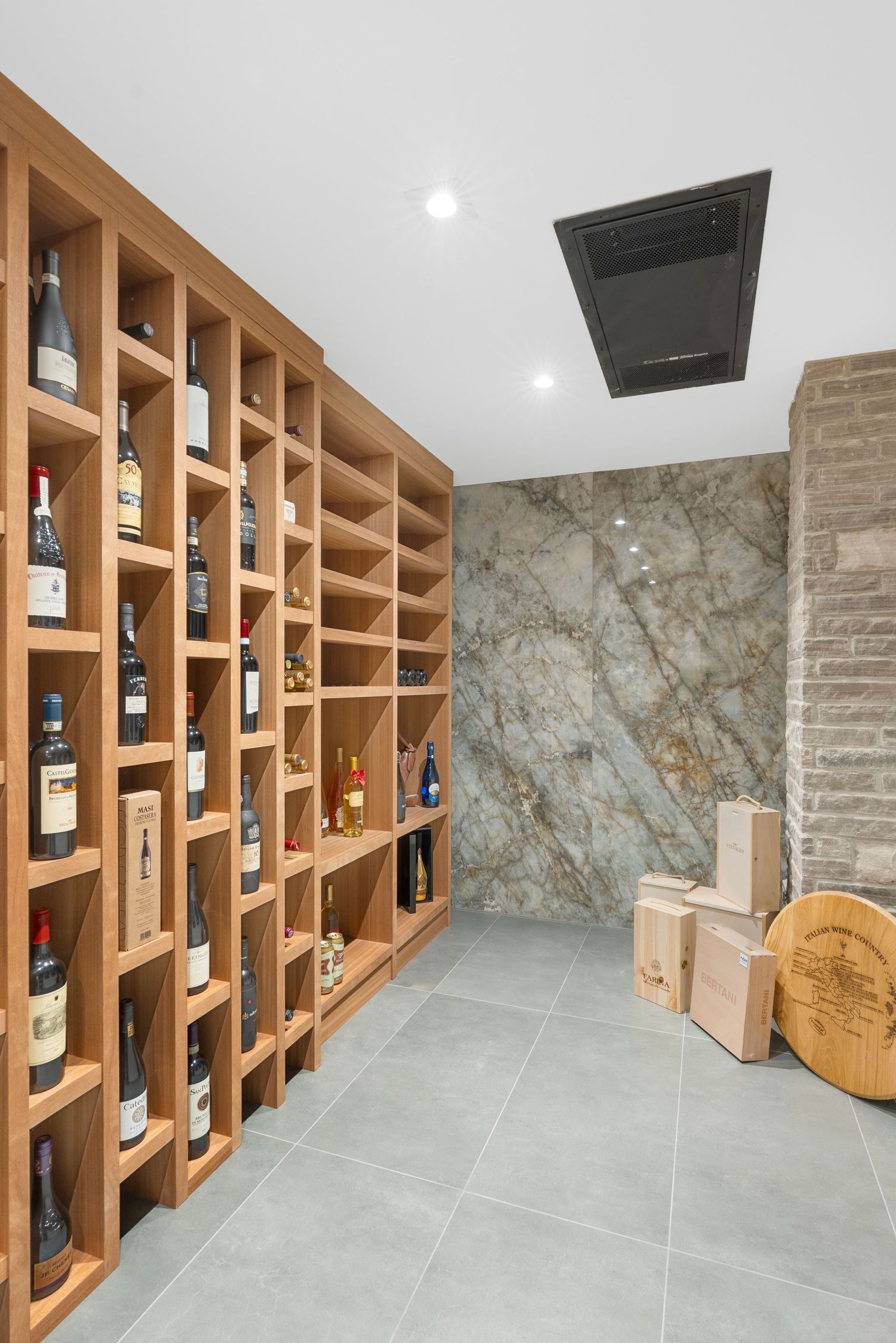 Wine cellar with wooden shelving units displaying collection of bottles against marble wall.