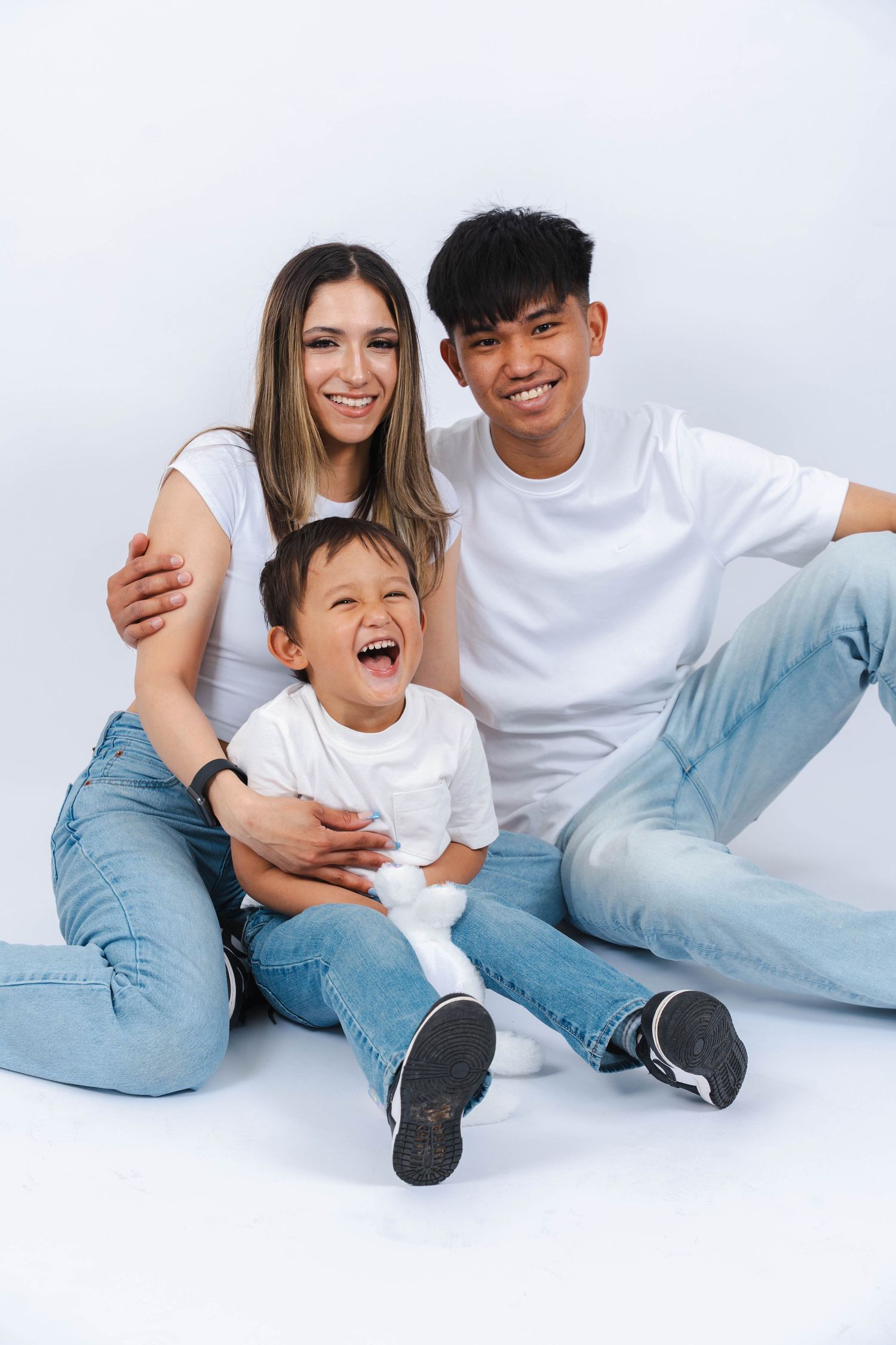 Family wearing white shirts and jeans playfully posing together on white background.