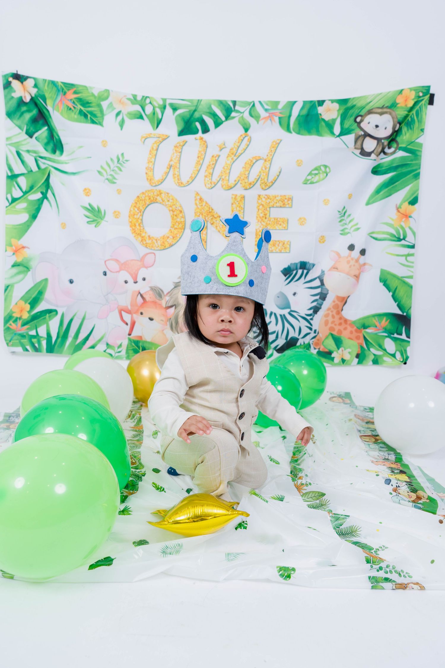 First birthday party setup with jungle theme backdrop, green balloons and 'Wild One' gold lettering decoration.