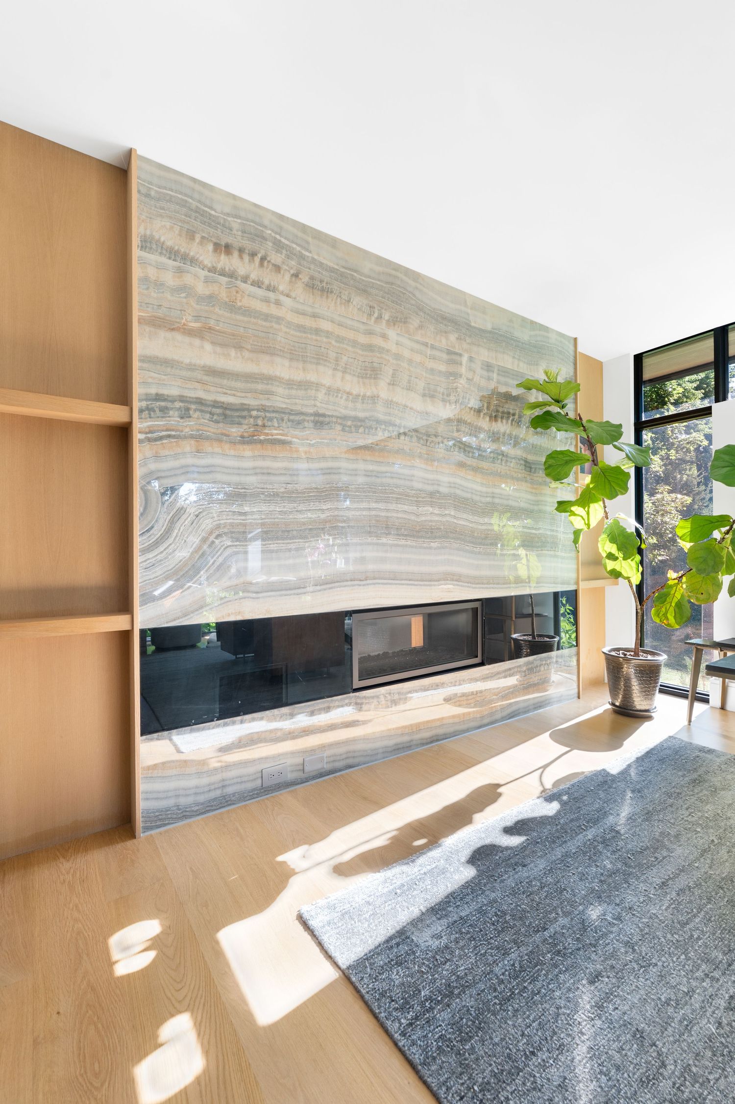 Sunlit modern space with marble accent wall and wooden shelving in minimalist design.