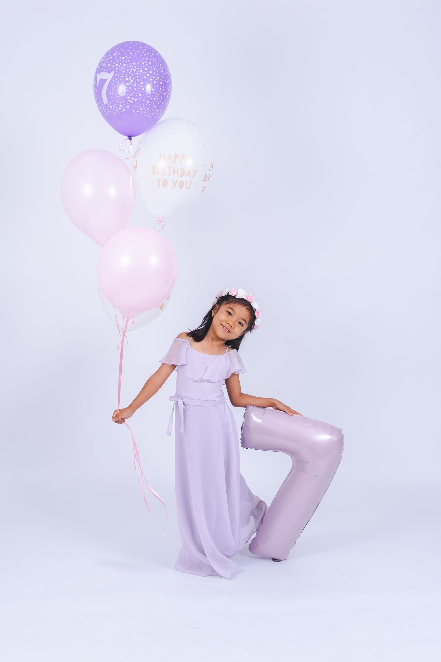 Artistic studio photoshoot with purple and pink balloons against light gray backdrop creating dreamy pastel aesthetic.