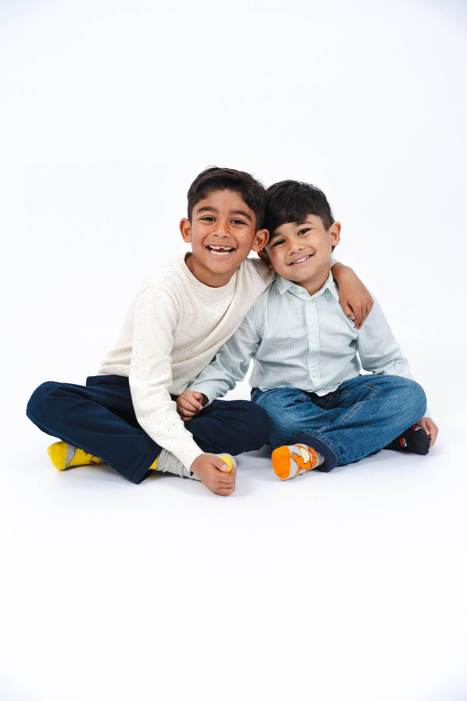 Two young children in white shirts and jeans sit close together on a white background in three playful poses.