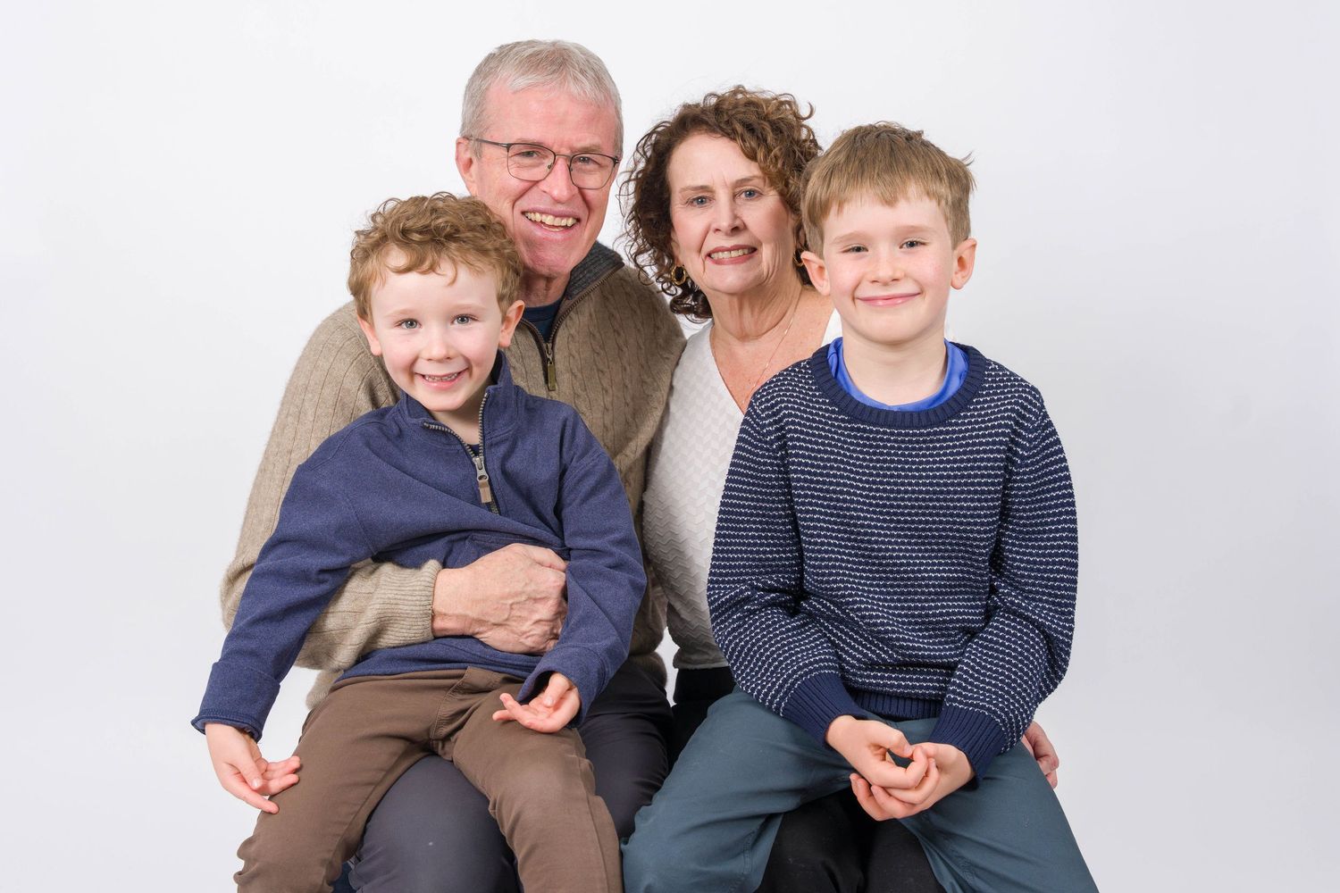 Multi-generational family members pose together against a light gray backdrop in matching blue and brown casual attire.