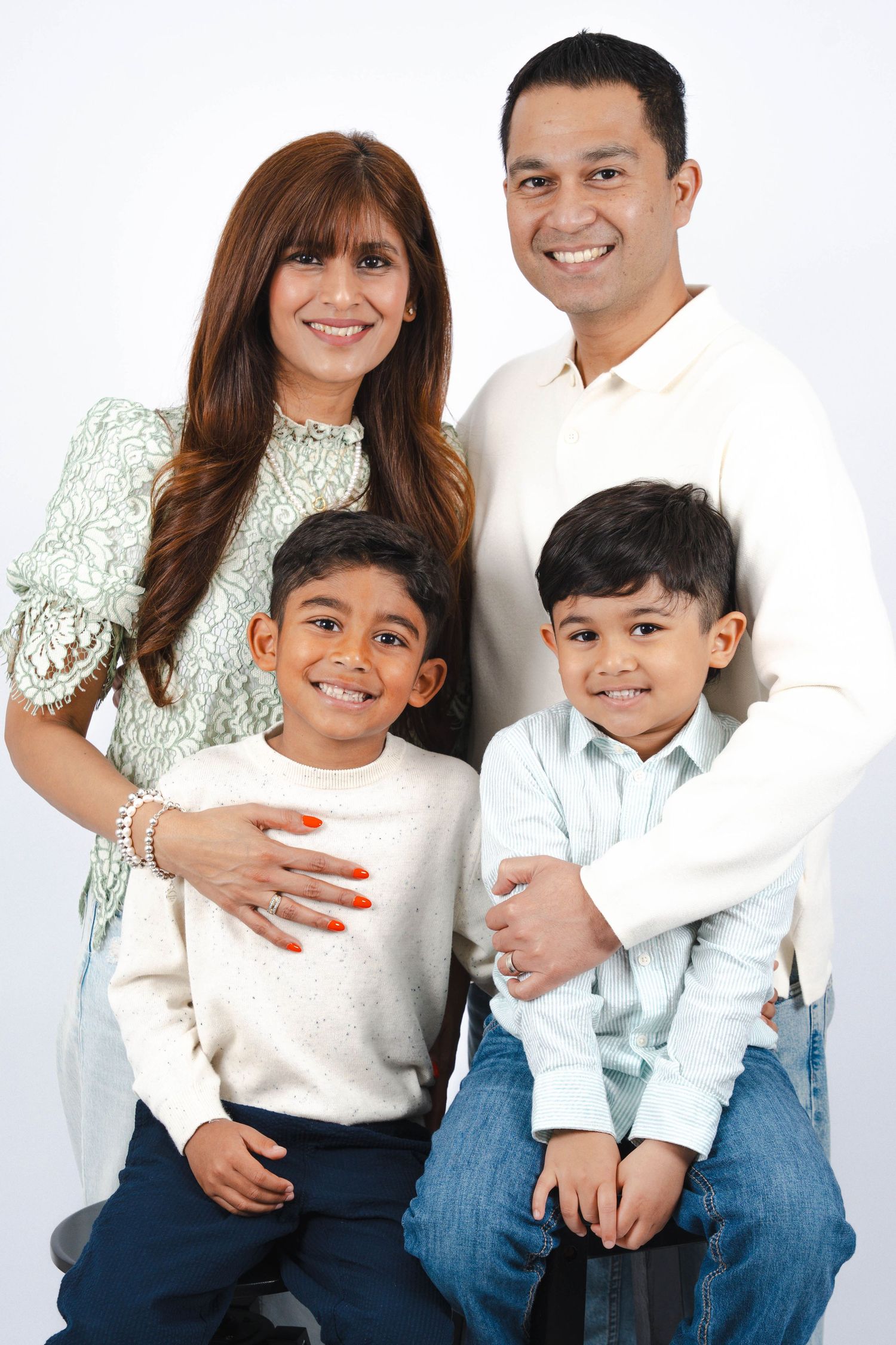 A happy family of four poses together against a white background in coordinated casual outfits.