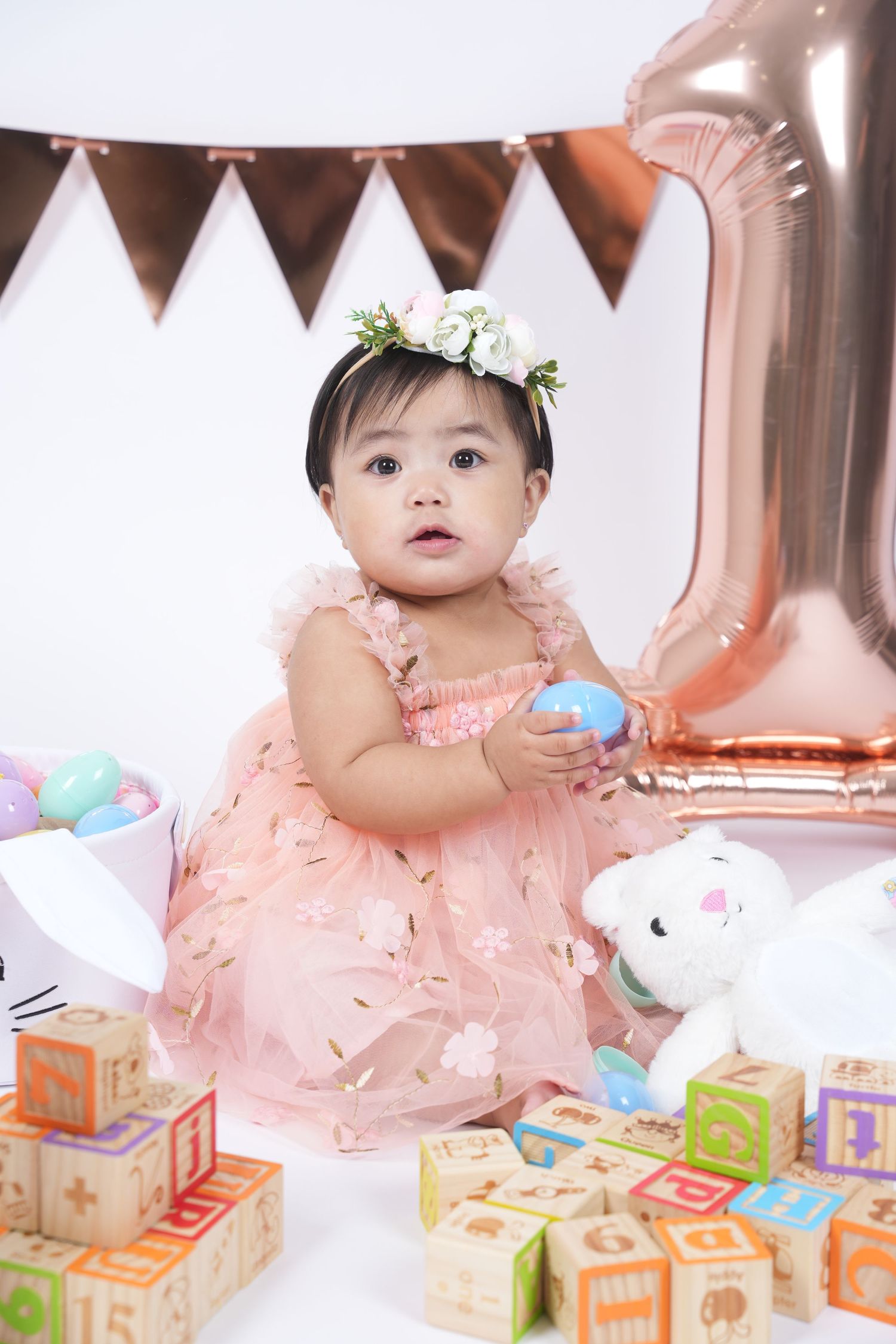 Baby in peach tulle dress plays with colorful alphabet blocks and plush bunny during indoor photo session.
