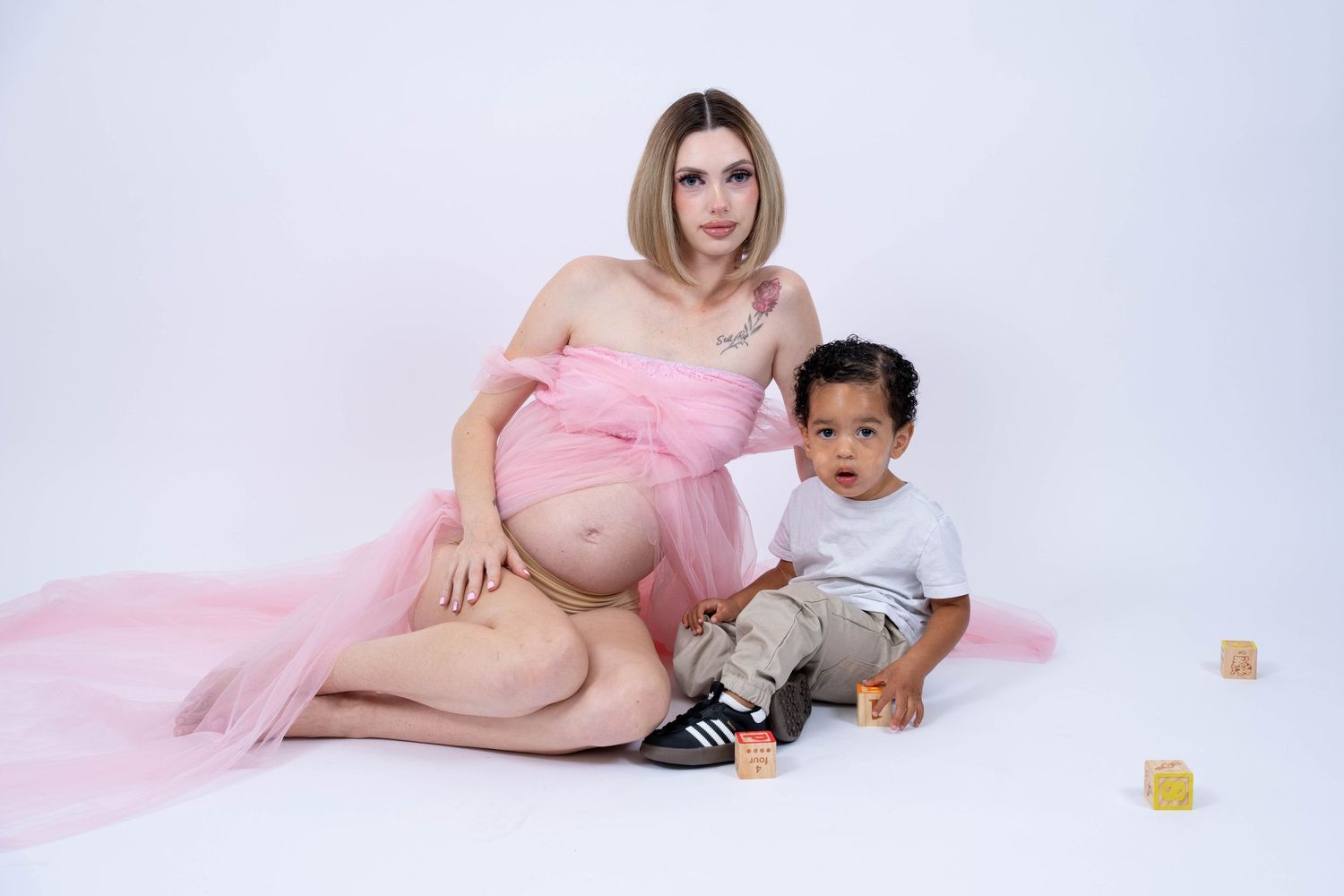 Maternity photoshoot featuring a pink flowing dress and gentle poses against a white backdrop.