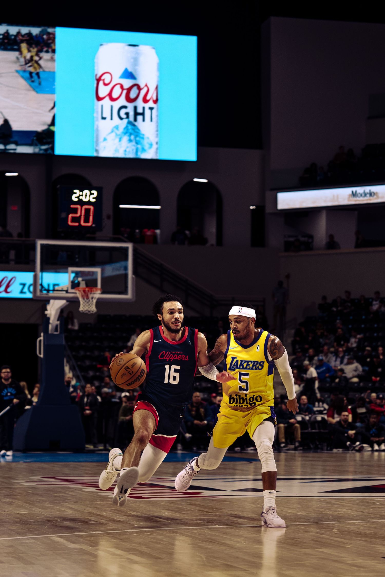Basketball players compete during a game with a Coors Light advertisement displayed on the scoreboard above the court.