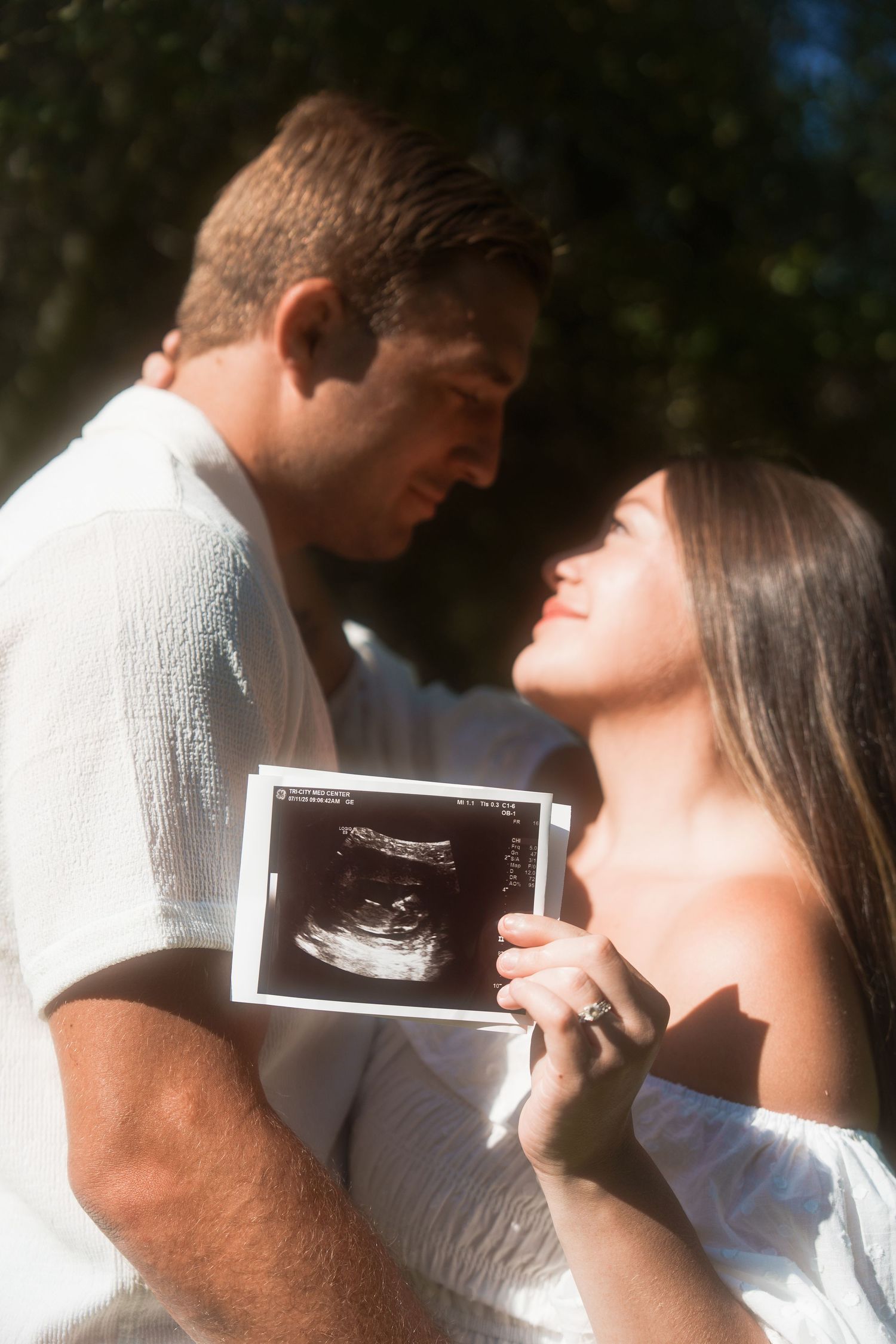 couple staring an one another with the girl showing off ultrasound for baby announcement.