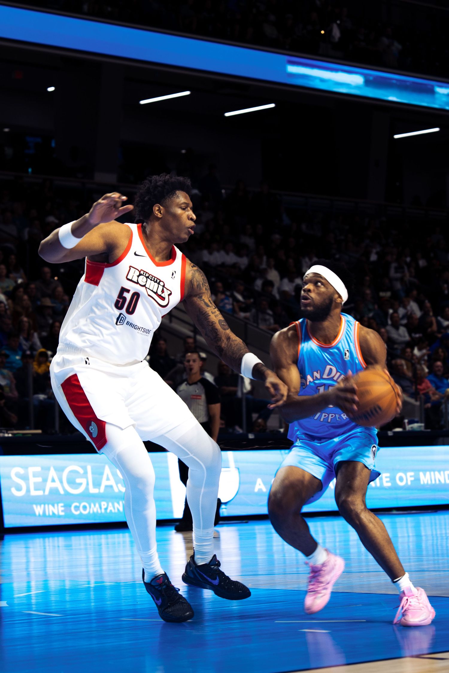 Two basketball players compete during a professional game with a blue illuminated court and Seagla signage visible.