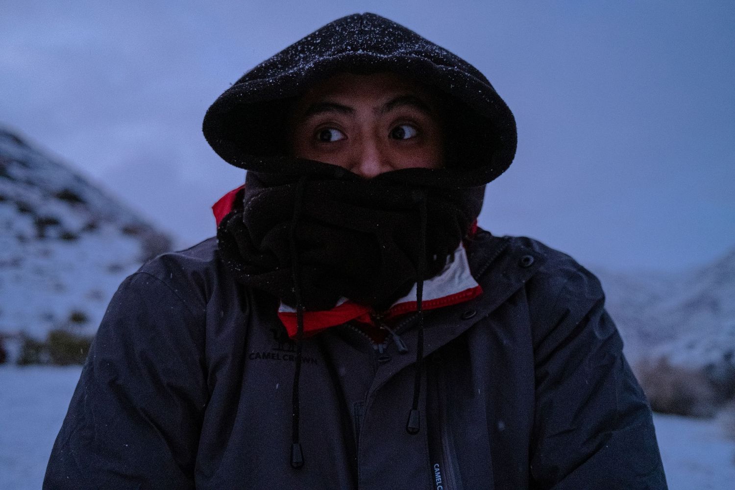 Figure in dark winter clothing and hat photographed against snowy blue backdrop.