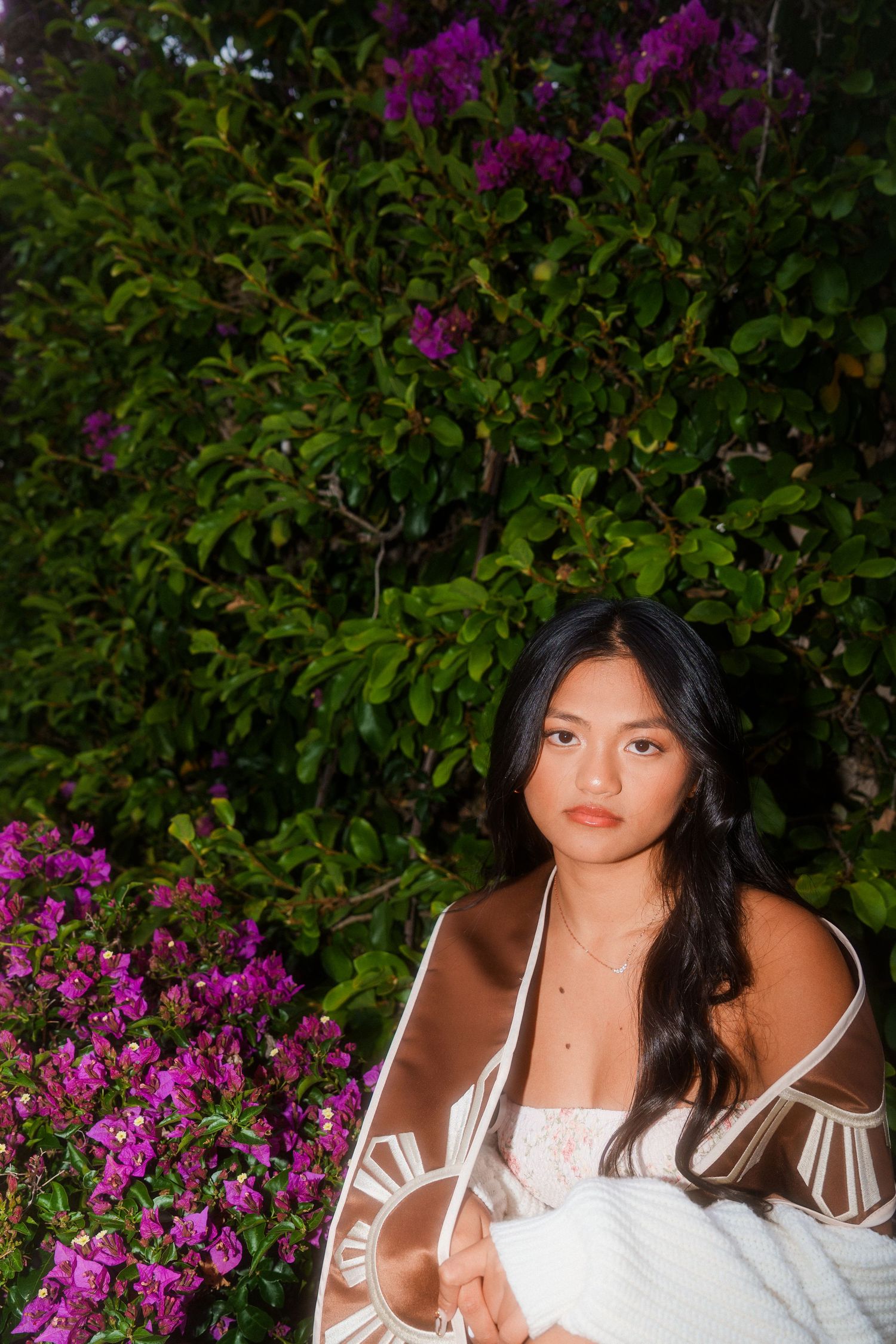girl squatting next to a bush looking at the camrea for a graduation photo