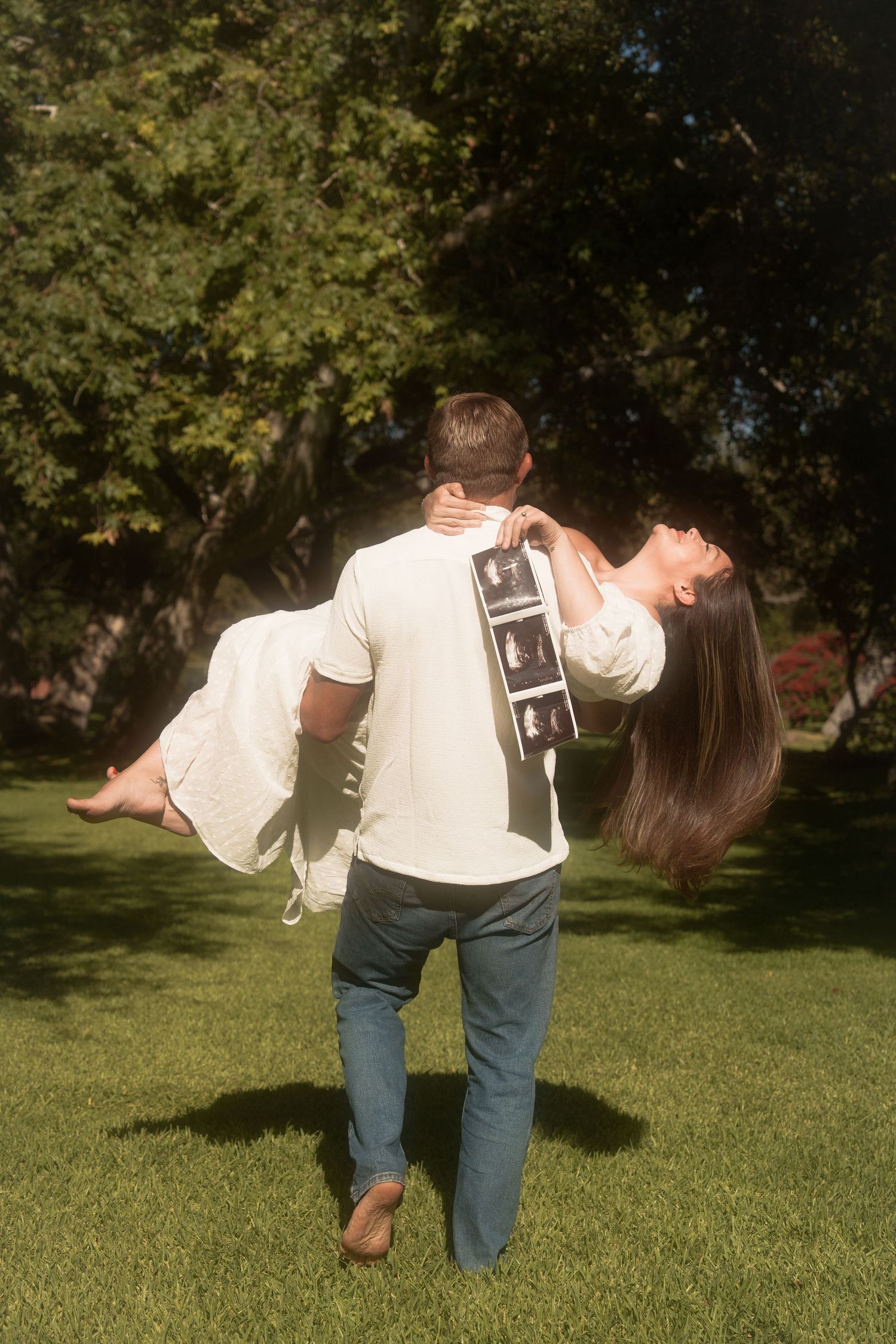 man holding woman with ultrasound photos for baby announcement photos