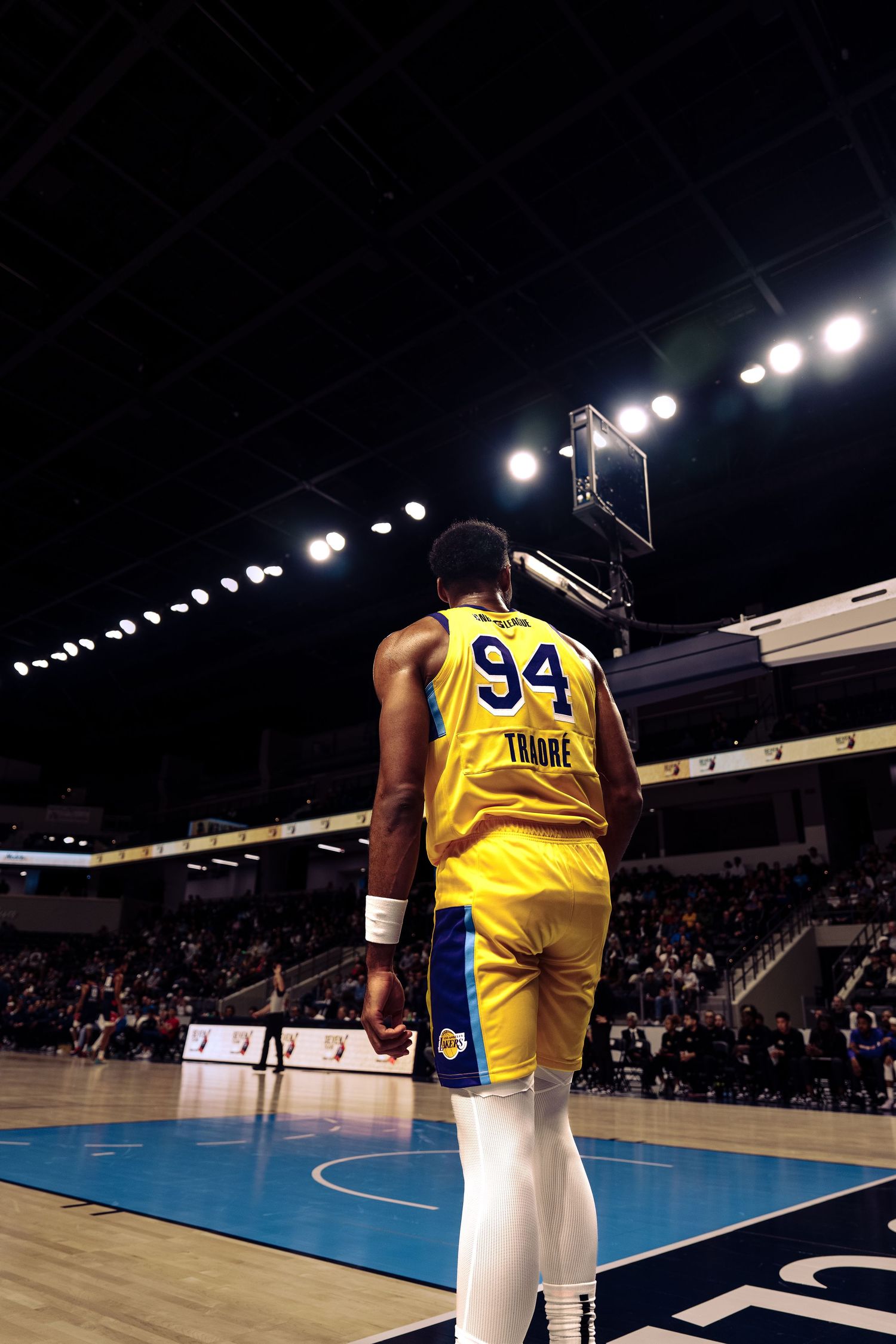 Basketball player in yellow jersey number 94 stands on court under arena lights during professional game.