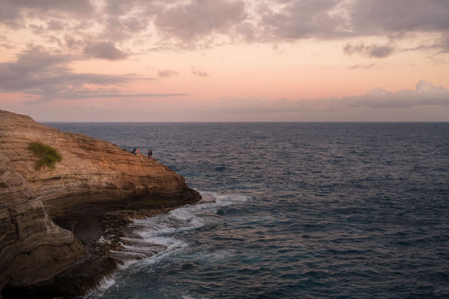Panoramic view of a rocky coastal cliff overlooking a vast ocean during a colorful sunset with scattered clouds. Hawaii Spitting Caves