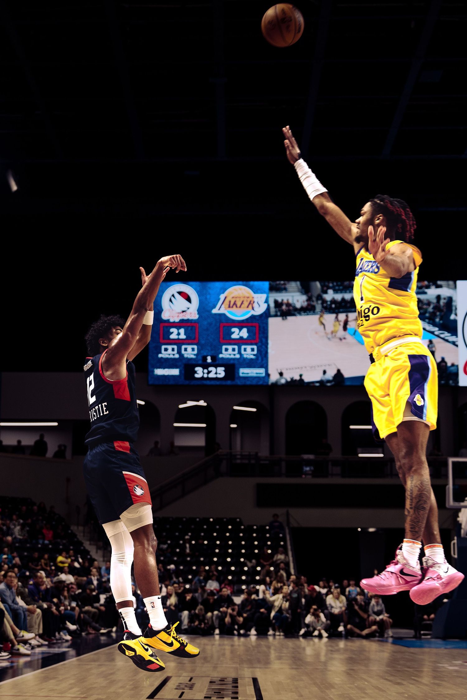 Two basketball players leap high in the air during a game, with one attempting to block the other's shot.