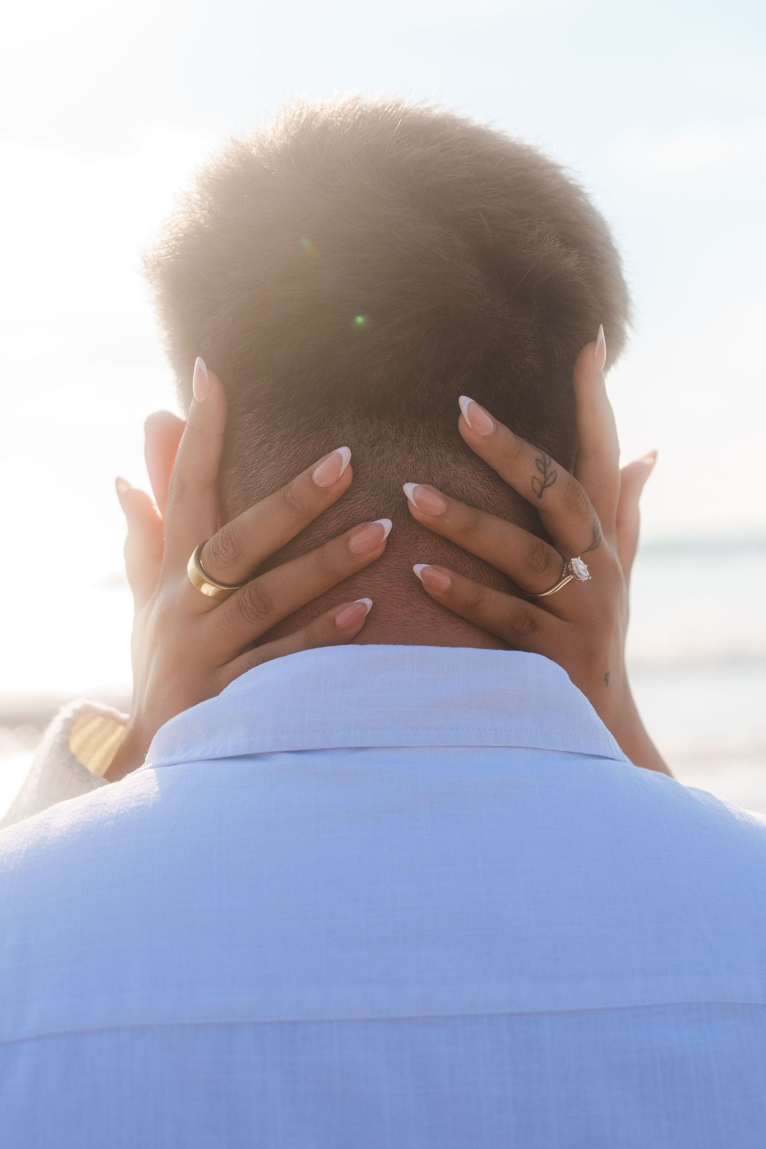 back of mans head with womans hands holding his neck with an engagement ring on her finger for a engagement photoshoot