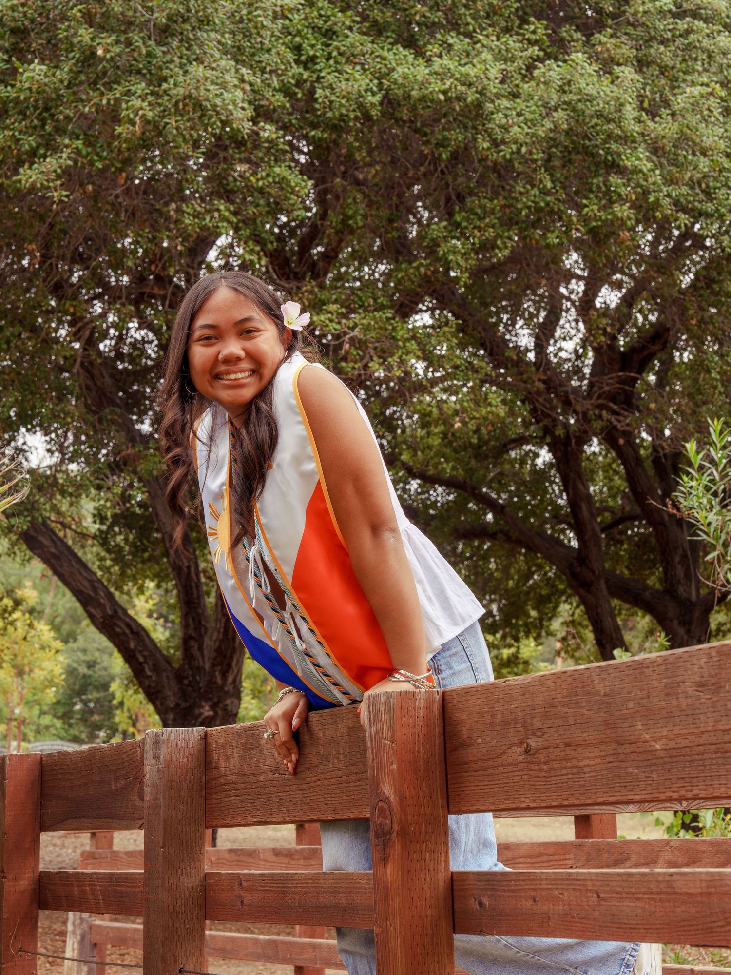 girl leaning along the railing of a wooden bridge wearing graduation filipino stole for a graduation photoshoot