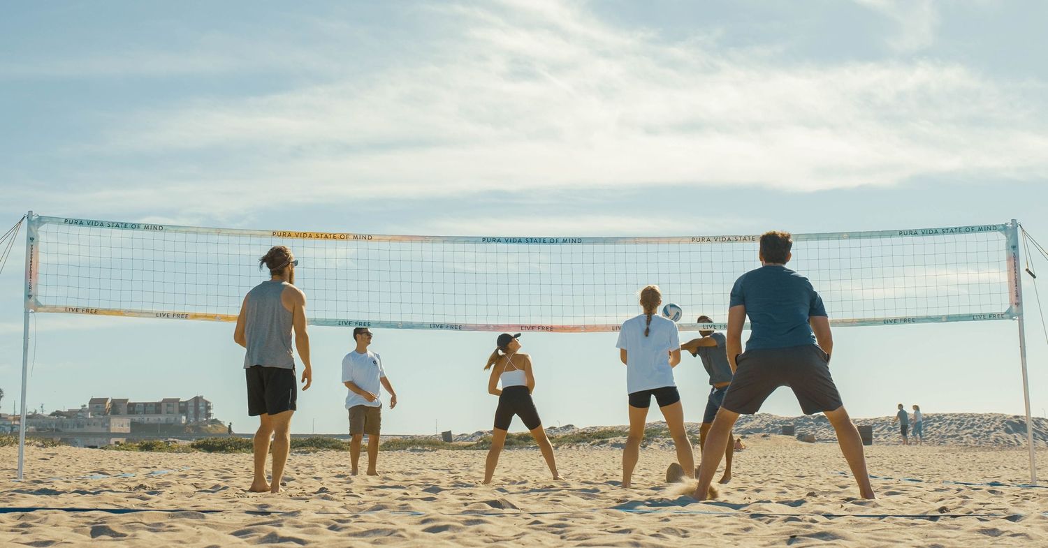 Group of friends playing beach volleyball on sandy shore under partly cloudy sky.