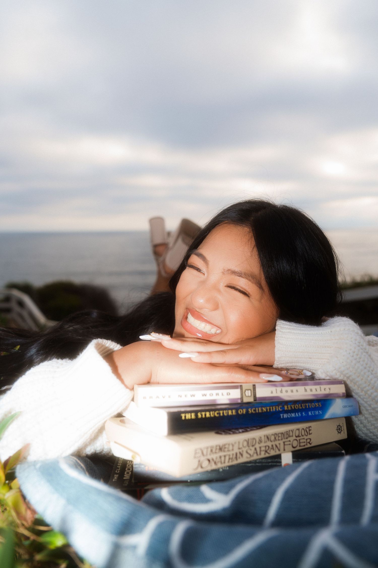 girl laying down on a blanket laying her chin on books for a graduation photo