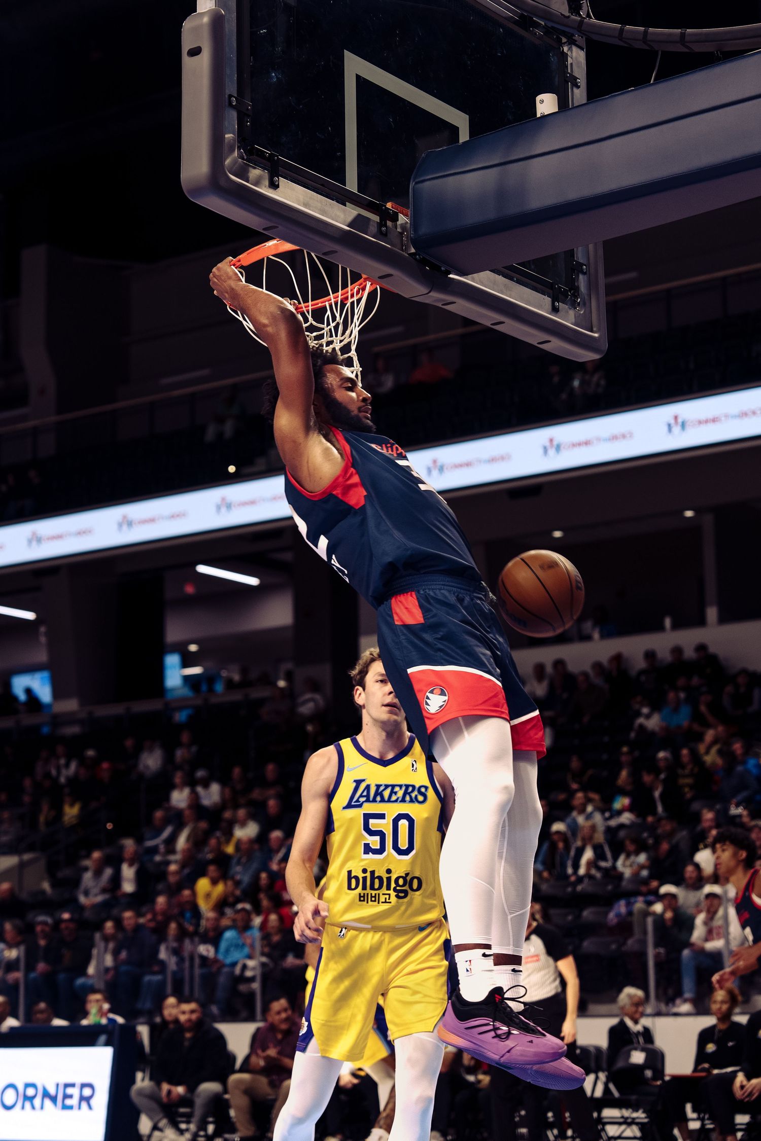 A basketball player in a Lakers jersey leaps for a slam dunk during an indoor game at a professional arena.