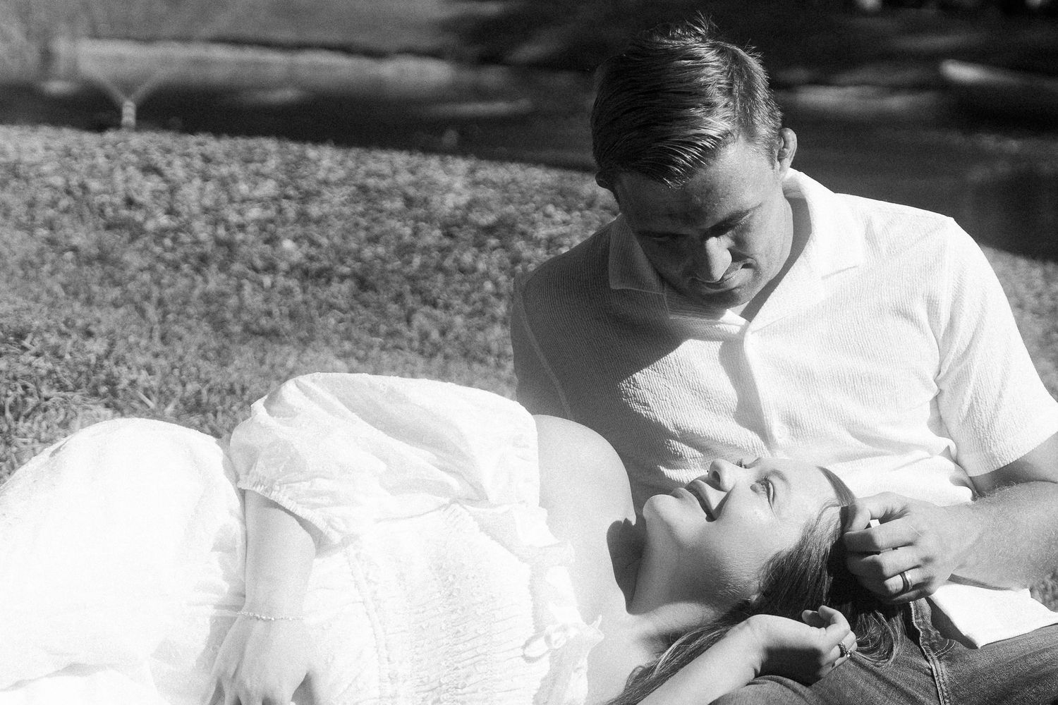 woman laying on mans lap while he sits in a dreamy baby announcement photoshoot