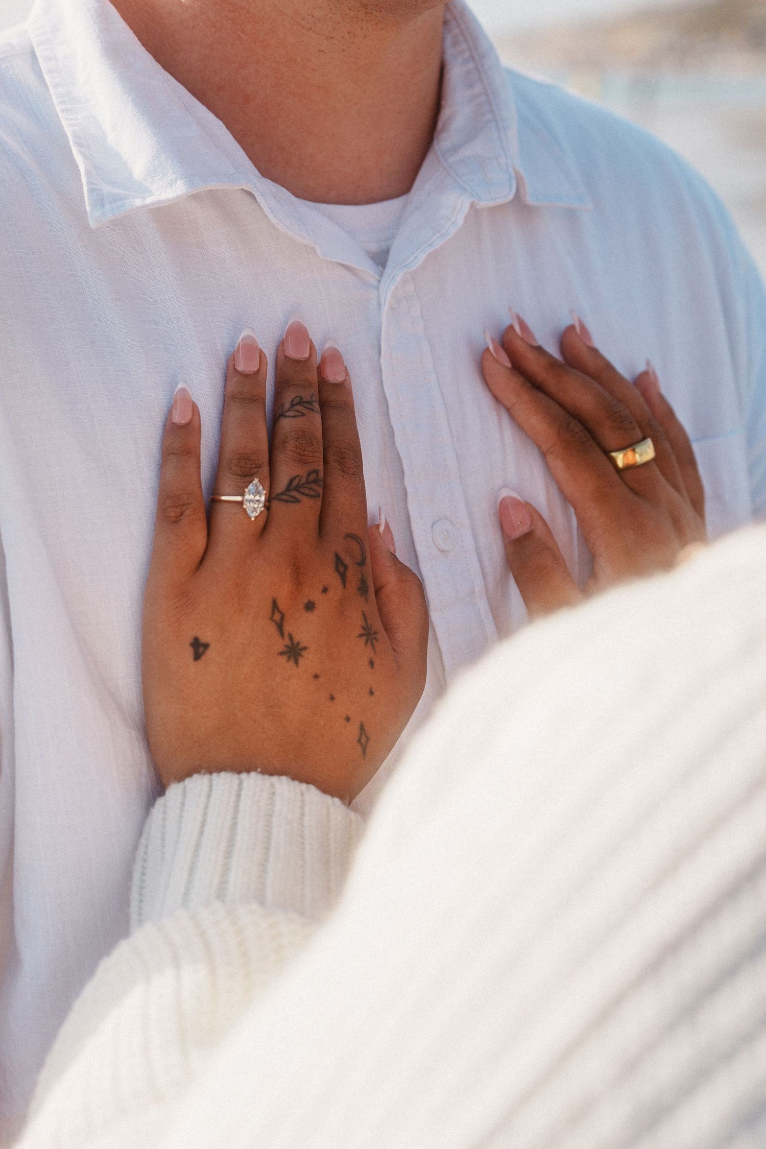 Small star tattoos and rings are displayed on a hand wearing a white sleeve.