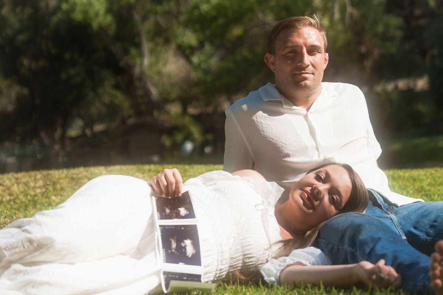 woman laying on mans lap while he sits in a dreamy baby announcement photoshoot