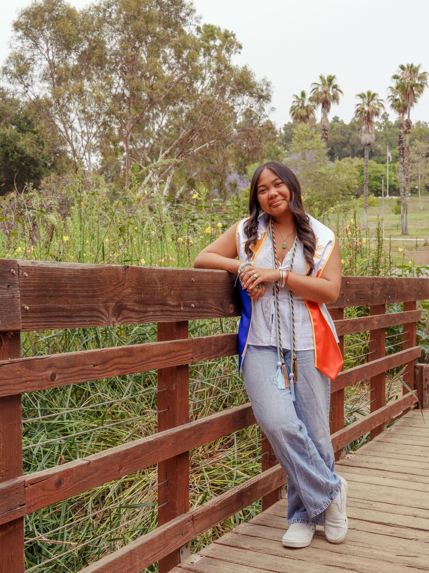 girl leaning along the railing of a wooden bridge wearing graduation filipino stole for a graduation photoshoot