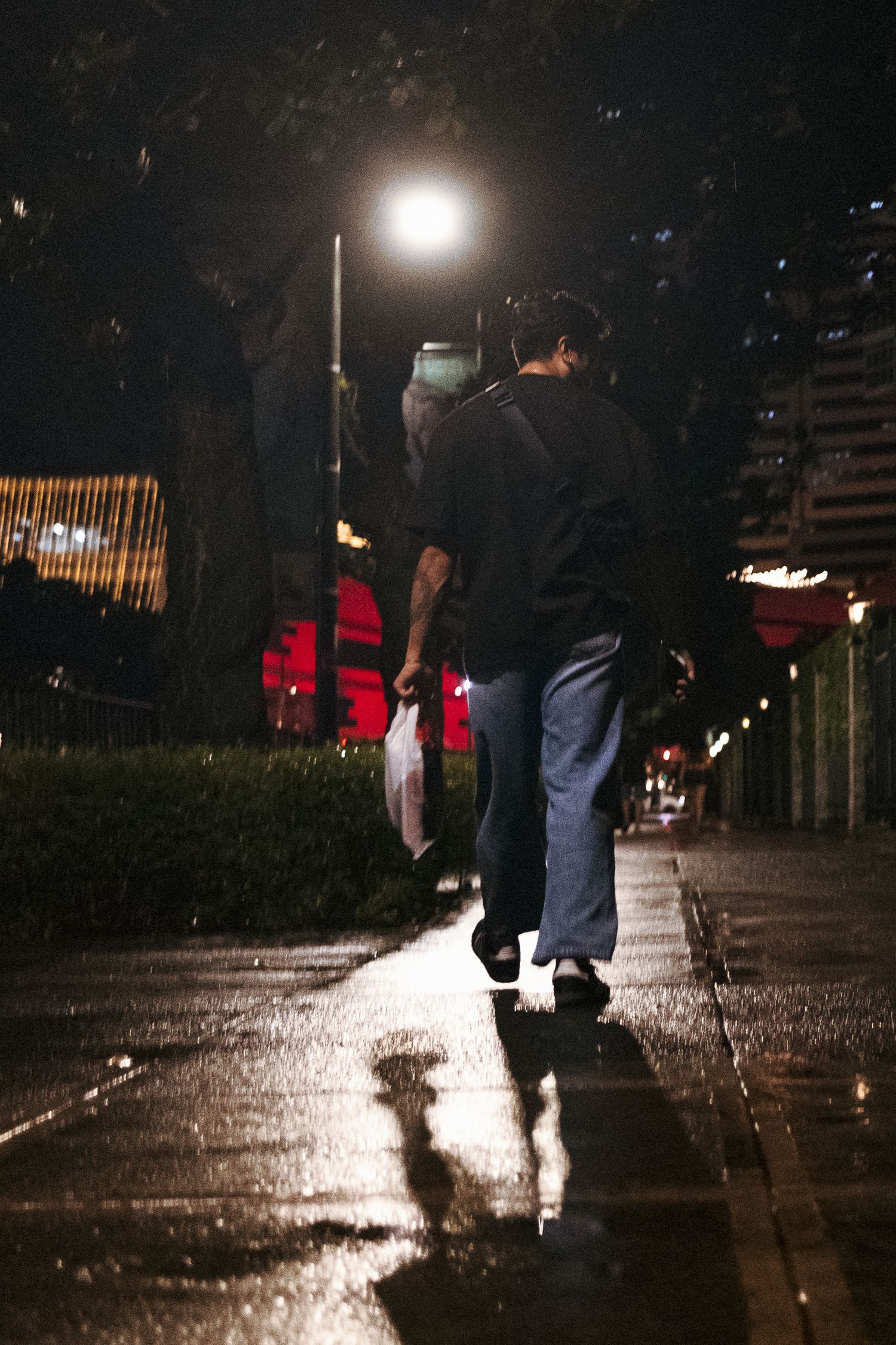 street photography photo of a man wearing jeans and a black shirt while its raining in manilla