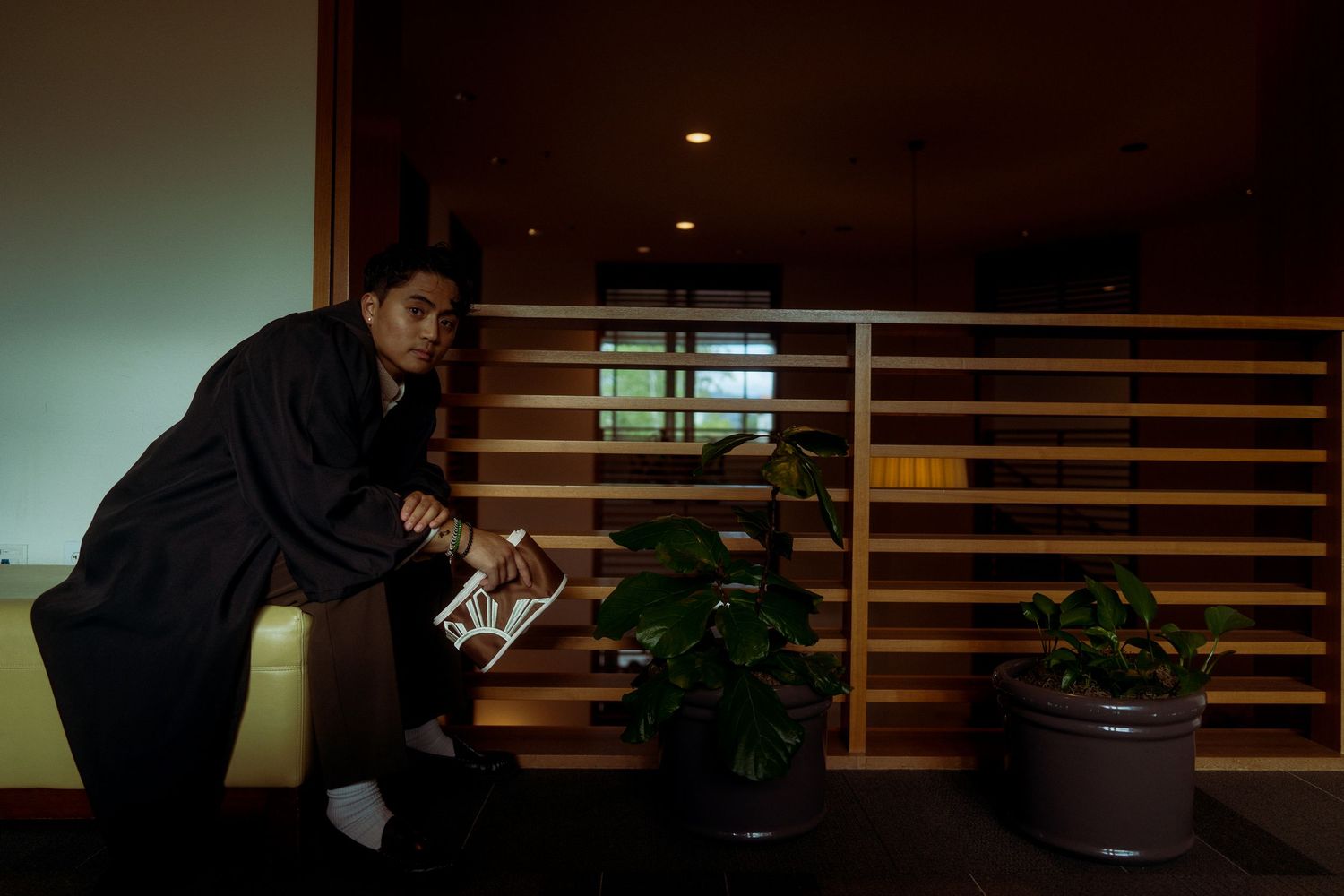 A Filipino male in graduation attire sits at a wooden bench for a Graduation shoot at the University of Redlands.