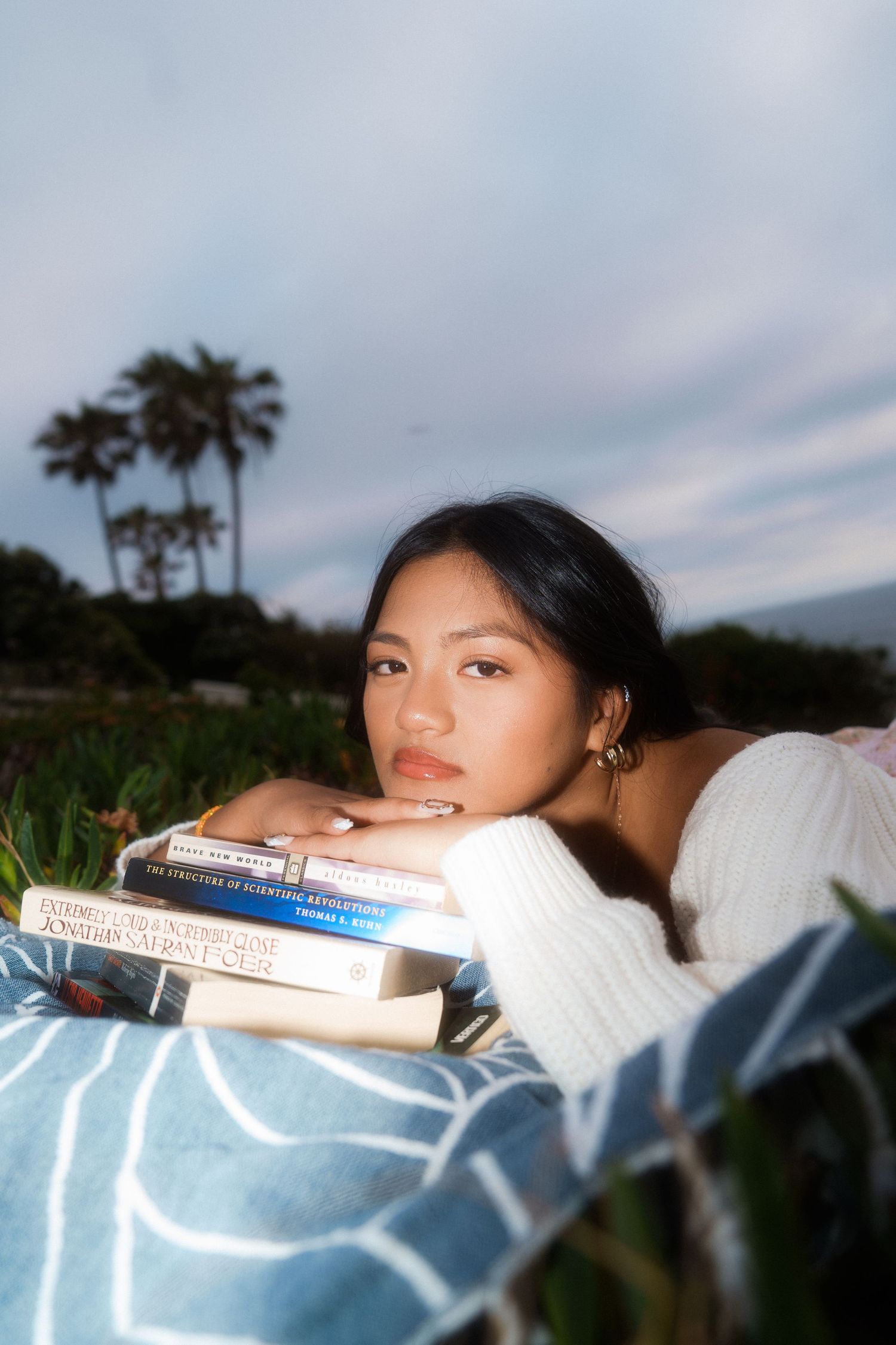 girl laying down on a blanket laying her chin on books for a graduation photo
