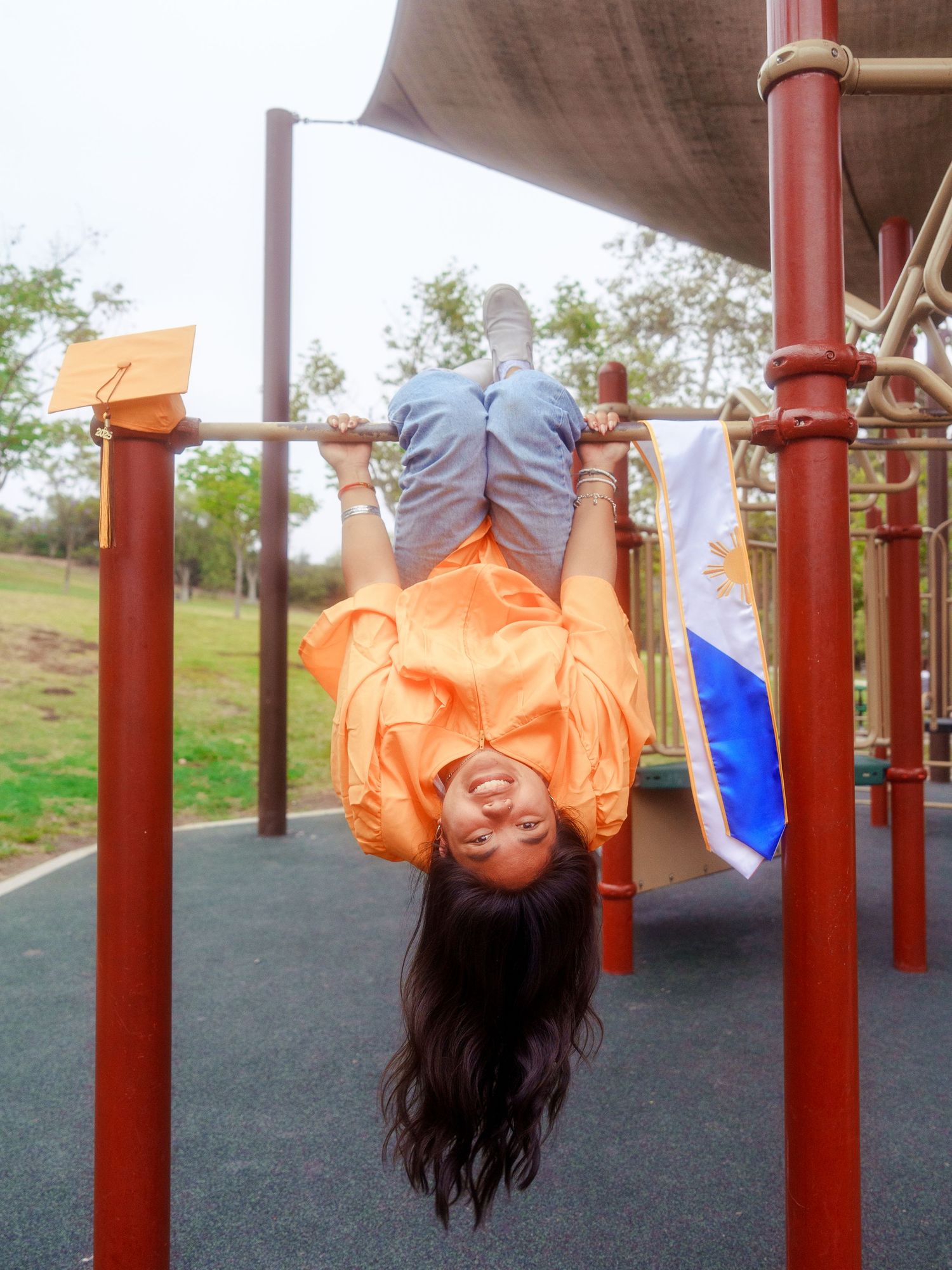 girl on monkey bars with a filipino stole for graduation posing uoside down for a graduation photo