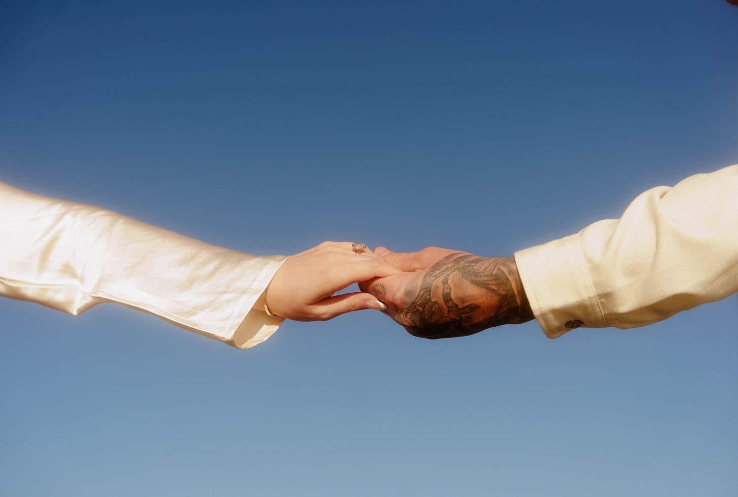 Two hands reach out to each other against a blue sky background in a symbolic gesture of connection and unity.