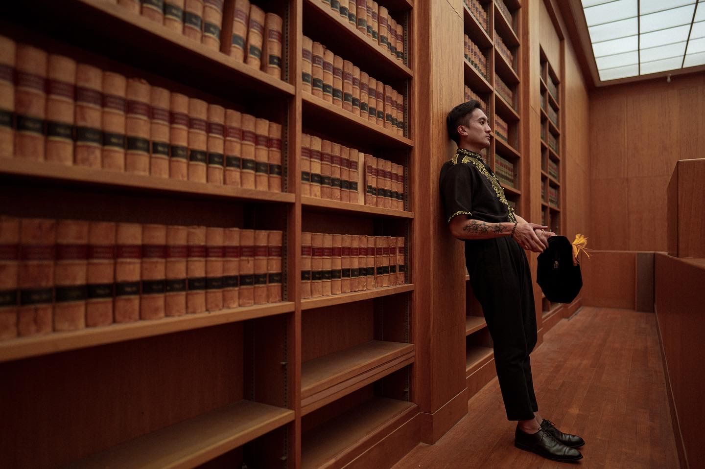 man leaning on bookshelf for a graduation photo, at UC Berkeley School of Law