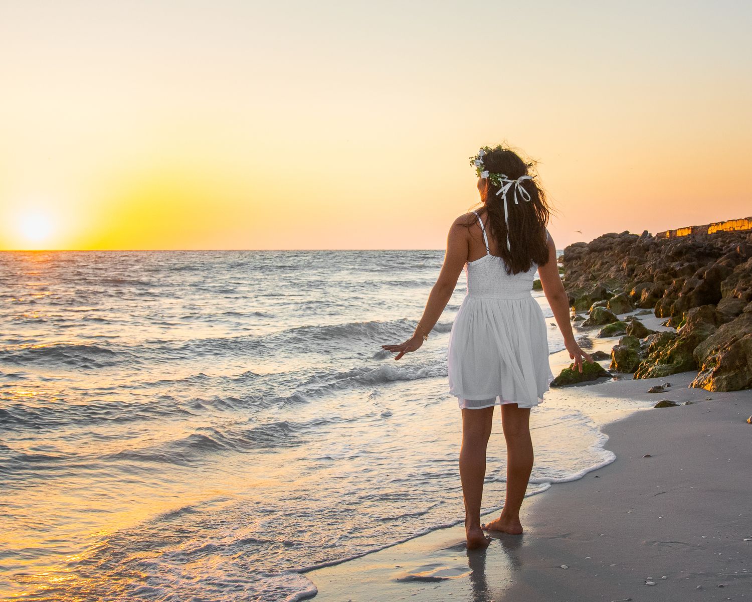 A girl looking off into the sunset while standing on the beach