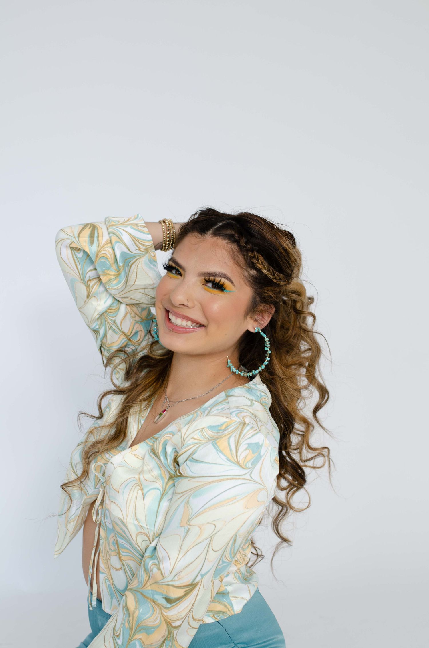 Smiling young woman with curly hair and turquoise accessories posing in a boho floral top.