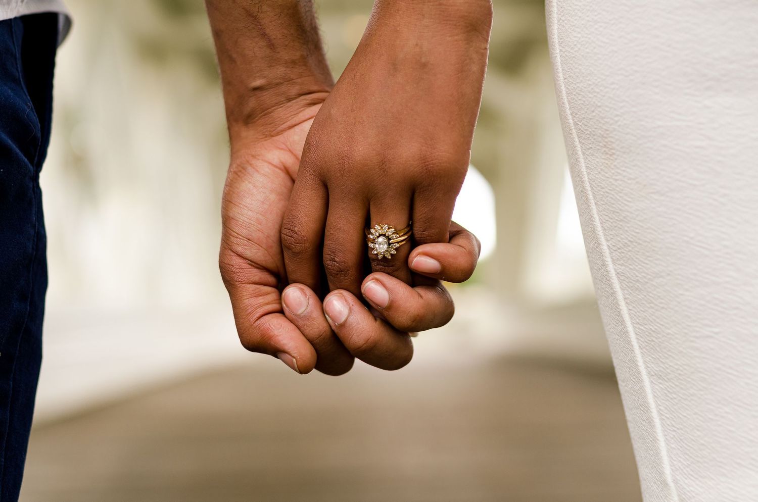 Close-up of an engaged couple holding hands, showcasing a beautiful diamond engagement ring.