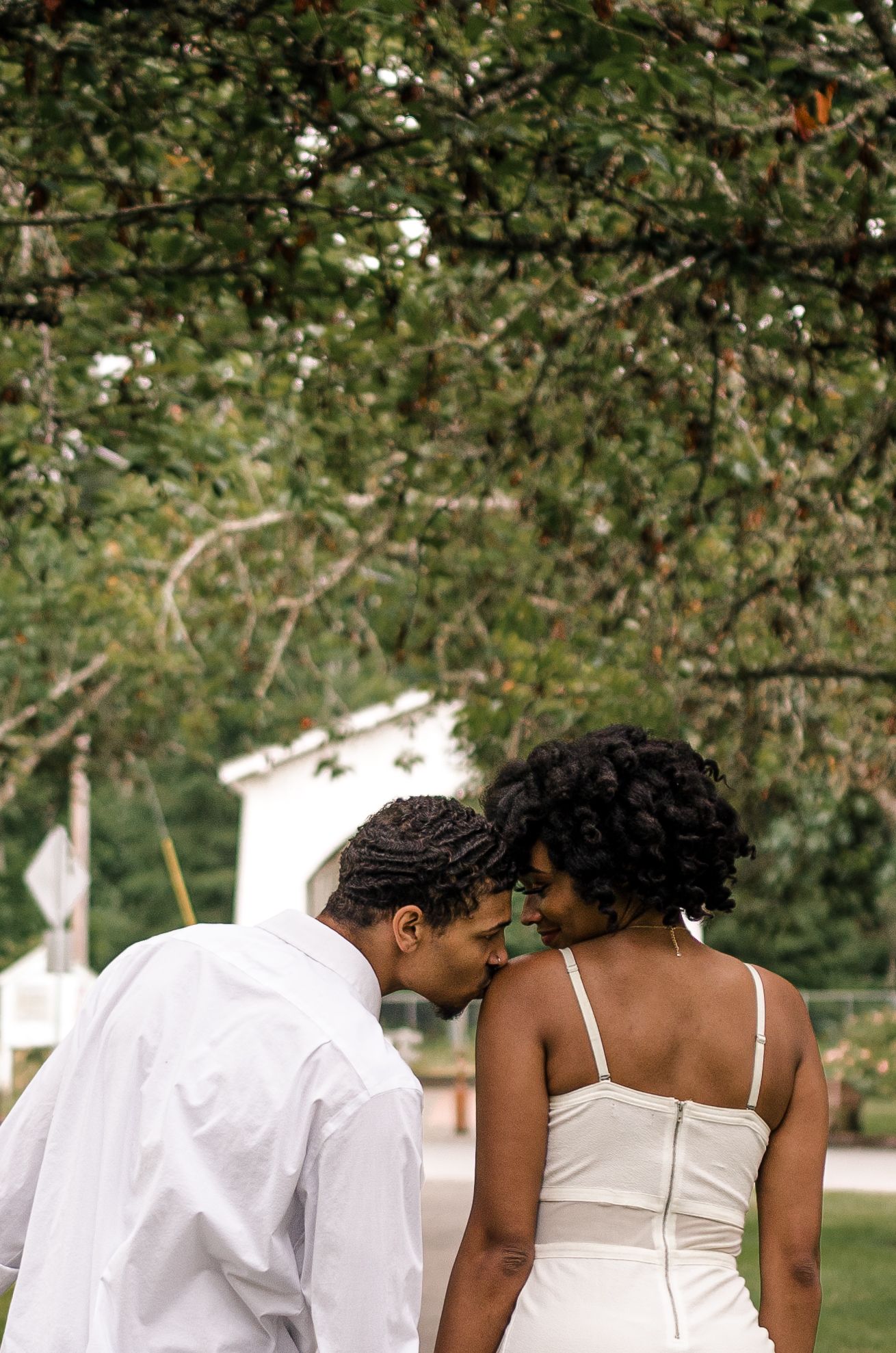 Bride and groom sharing an intimate forehead touch moment outdoors beneath lush green trees.