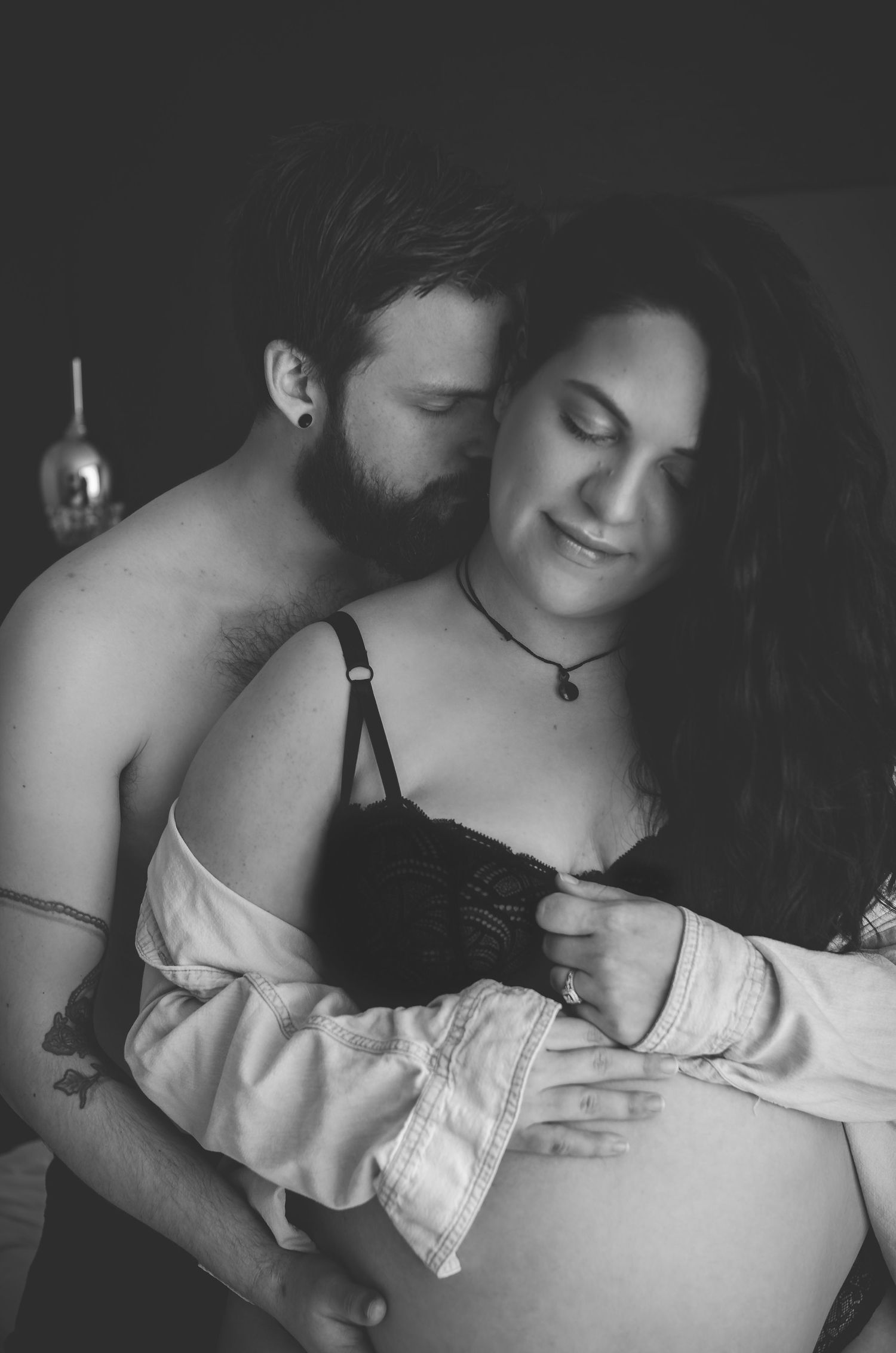 Black and white maternity photo of couple embracing, man kissing pregnant womans head while cradling her bare belly.