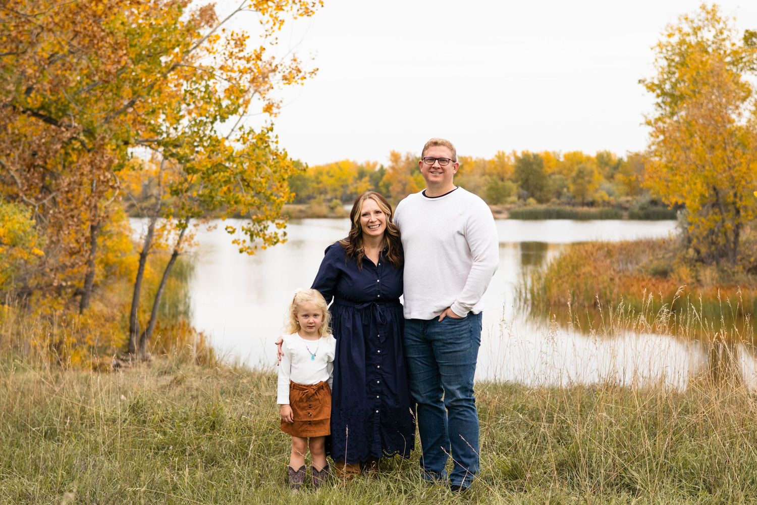 Family portrait in autumn setting with lake and golden trees in background.