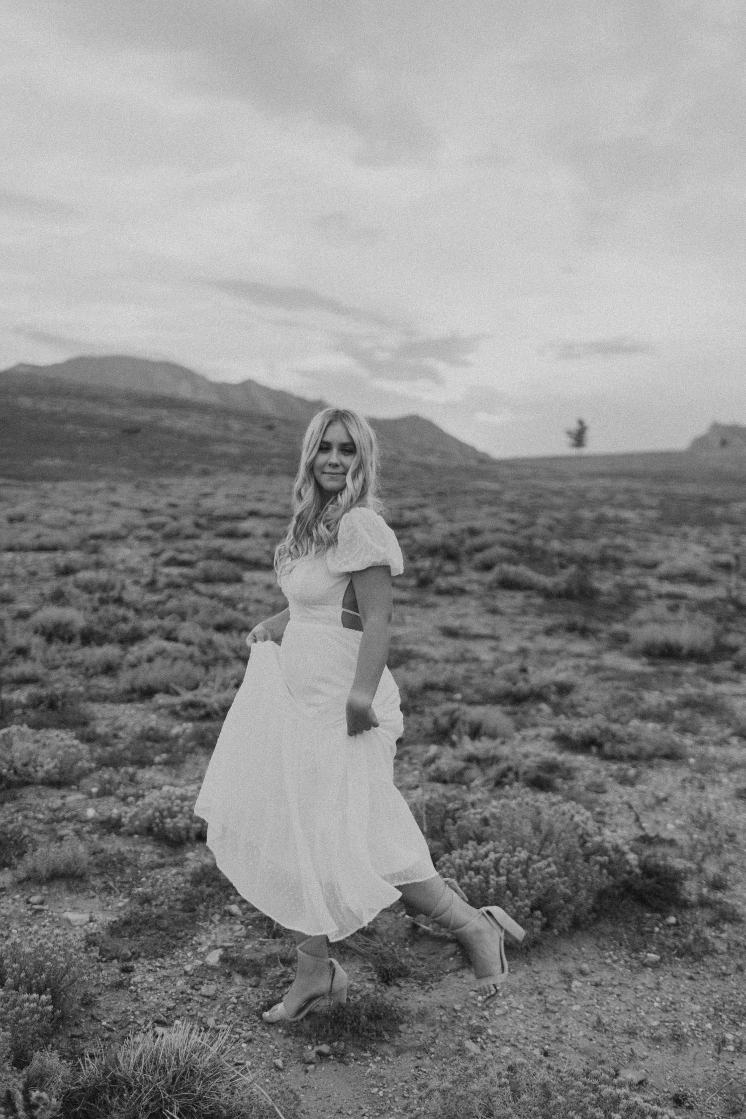 Black and white photo of woman in white dress on desert terrain.