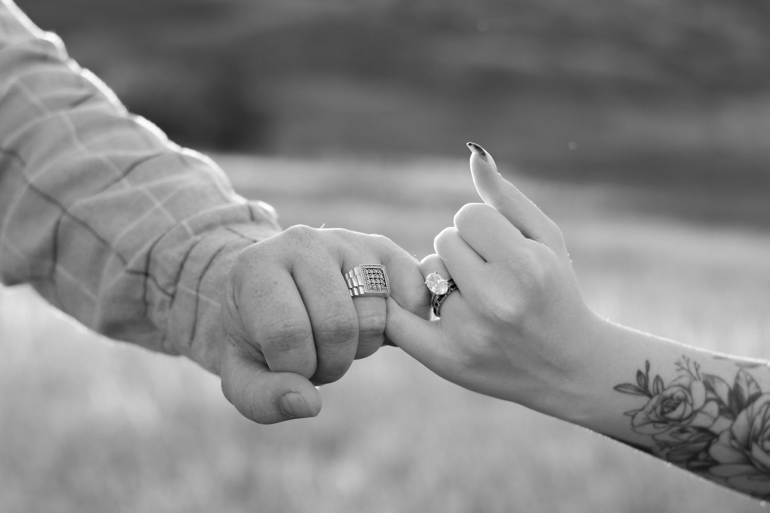 Close-up of hands with tattoos reaching towards each other against a blurred background.