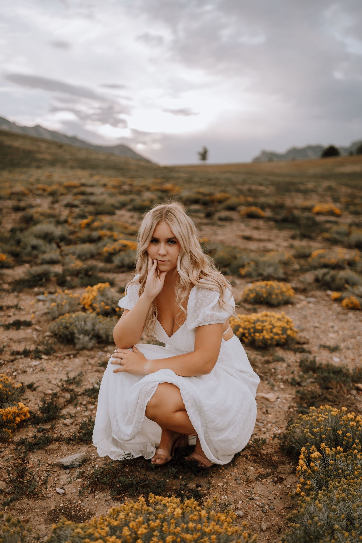 Woman in white dress poses in desert landscape with yellow wildflowers.