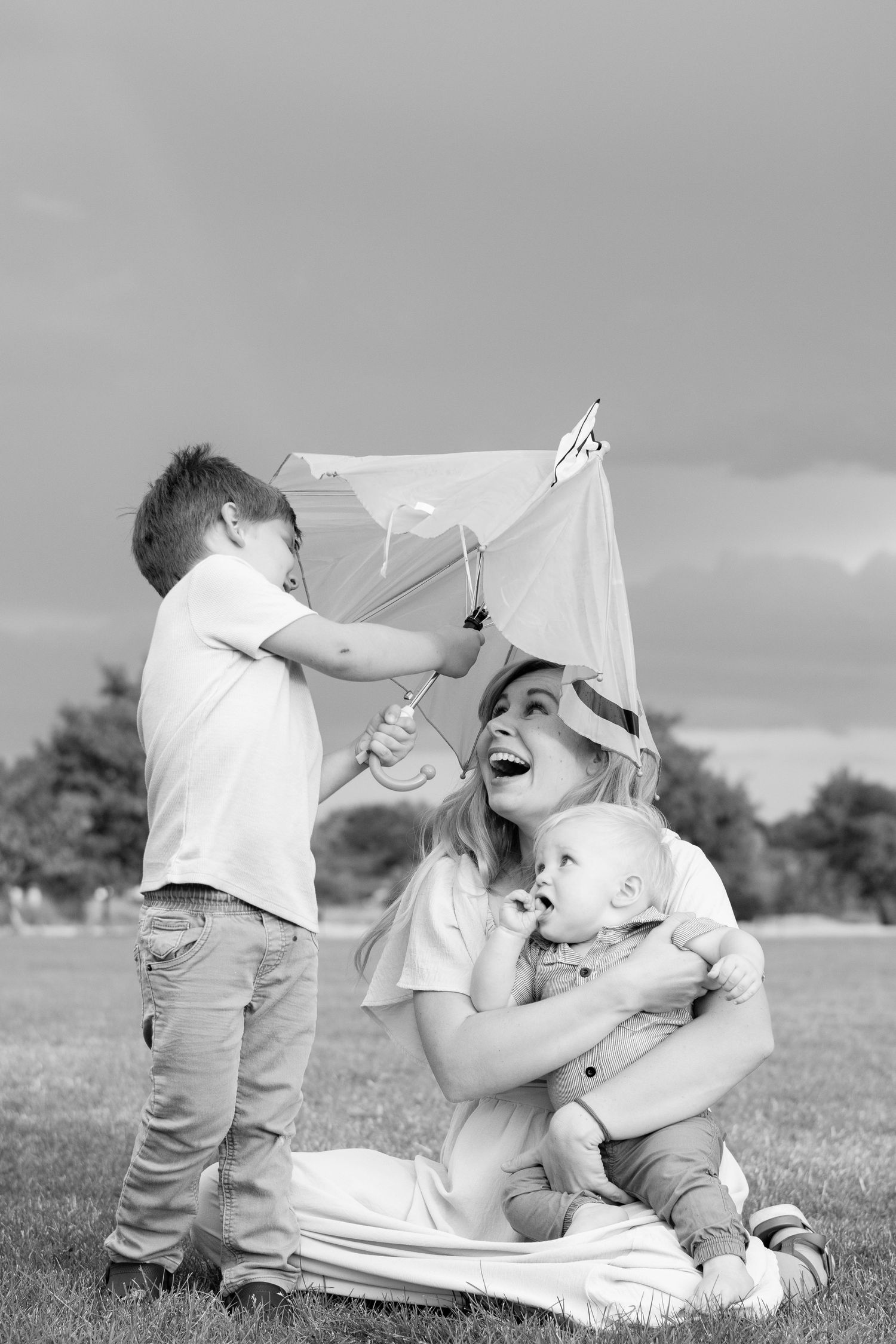 Black and white photo of playful moment with kite flying on grassy field.