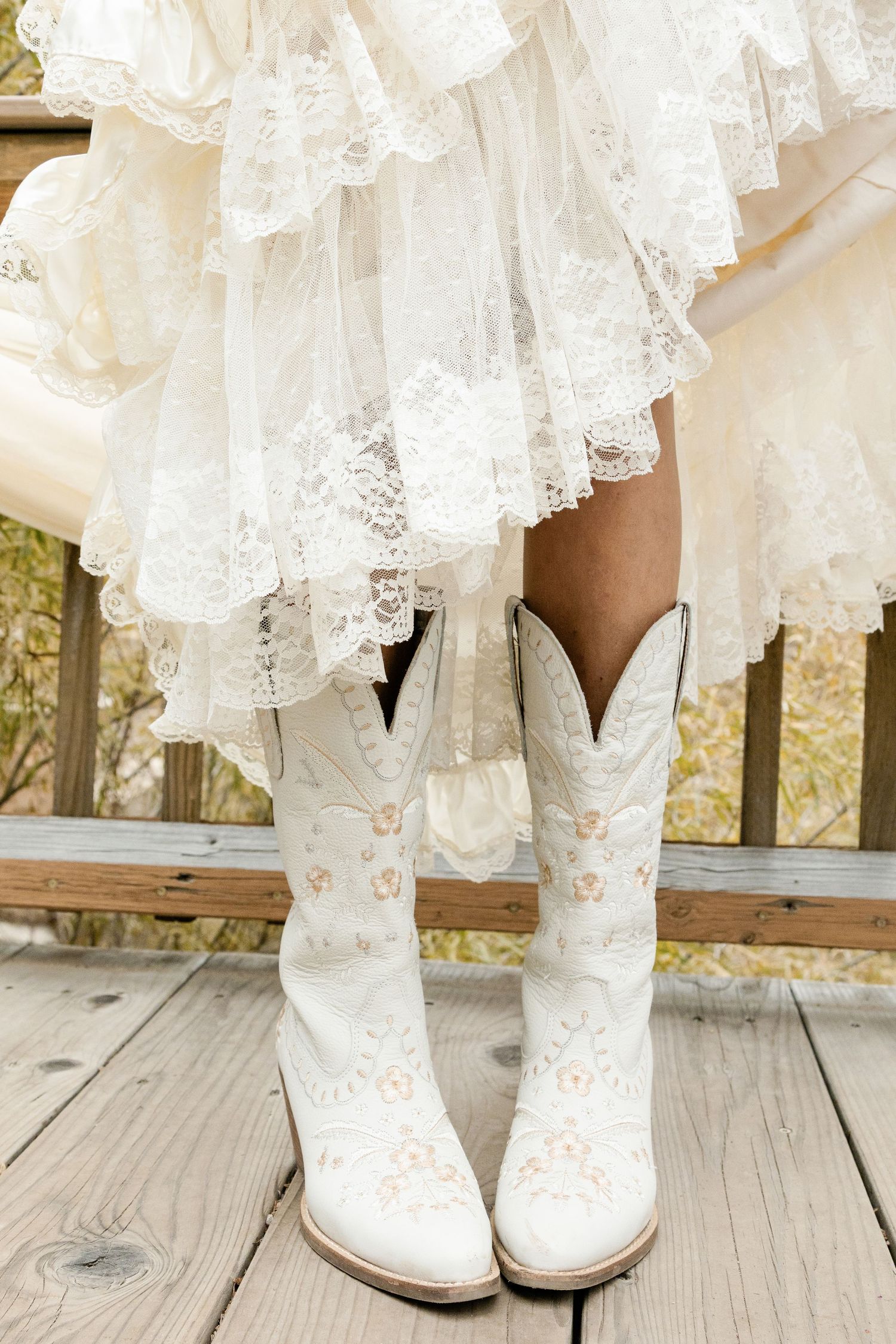 White lace wedding dress hem and cowboy boots on a wooden deck.