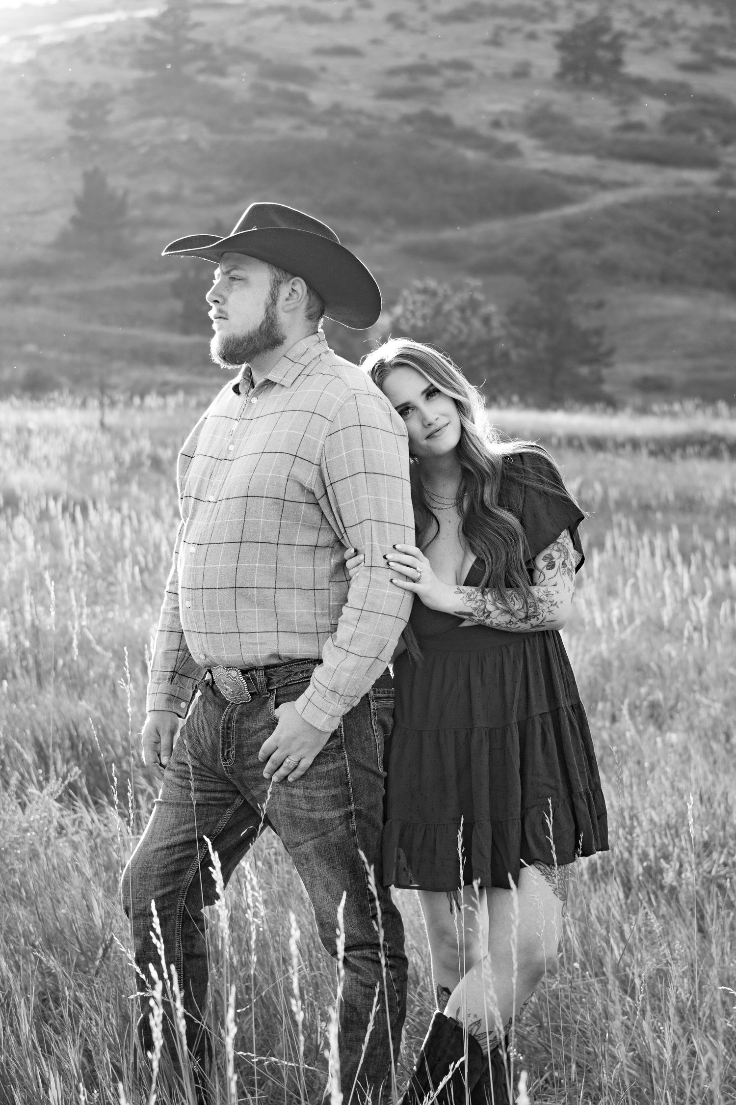 A romantic couple embracing in a field of tall grass with mountains in the background.