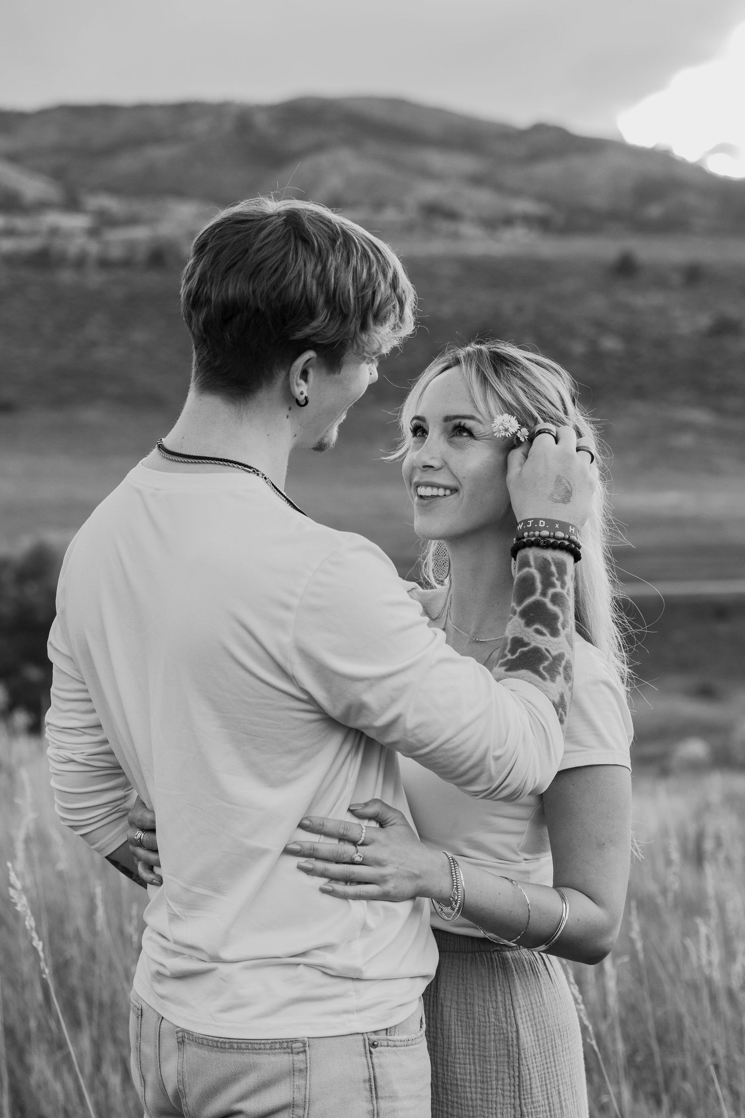 Black and white photo of couple dancing in mountain meadow wearing casual summer attire.